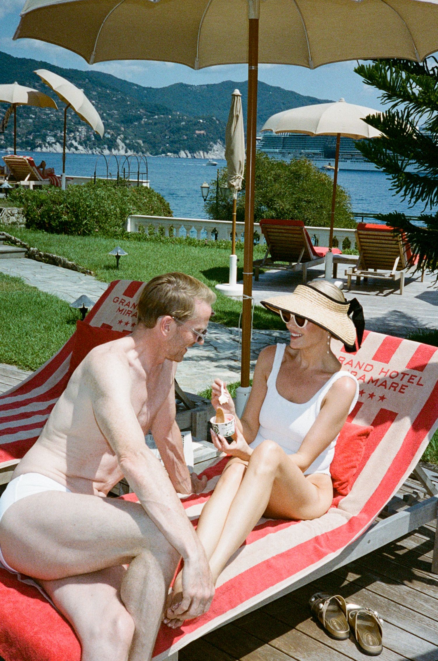 Couple relaxing on red lounge chairs at Grand Hotel del Mare with stunning Italian Riviera sea views.