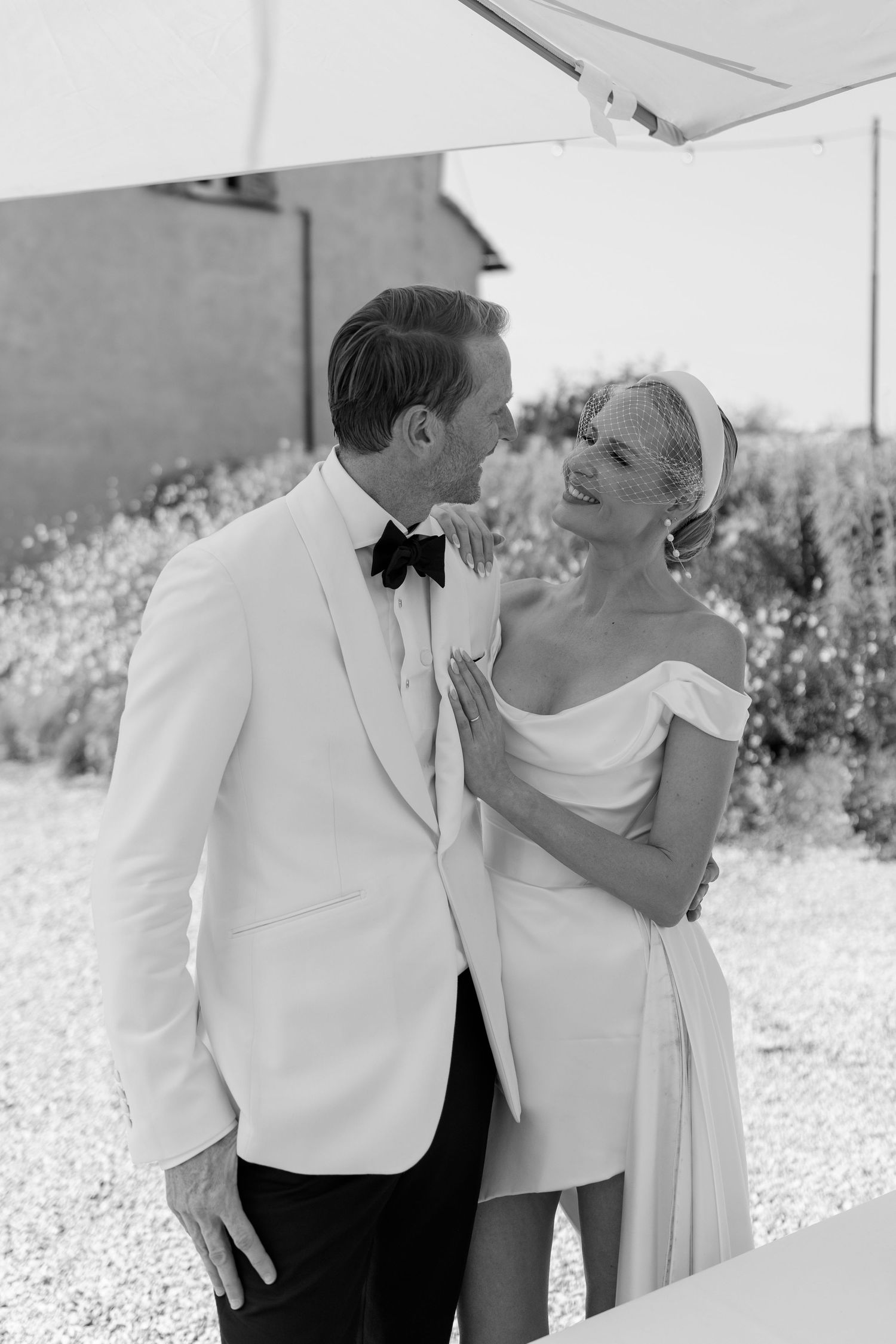 Elegant bride and groom in white tuxedo sharing a tender moment at outdoor wedding.