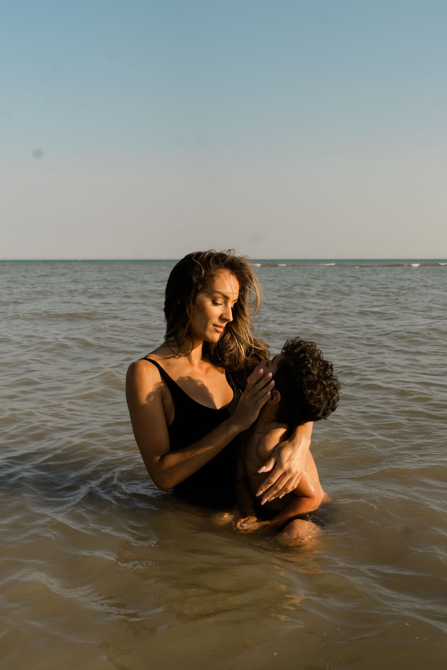 A tender moment shared between two people in calm ocean waters at sunset.