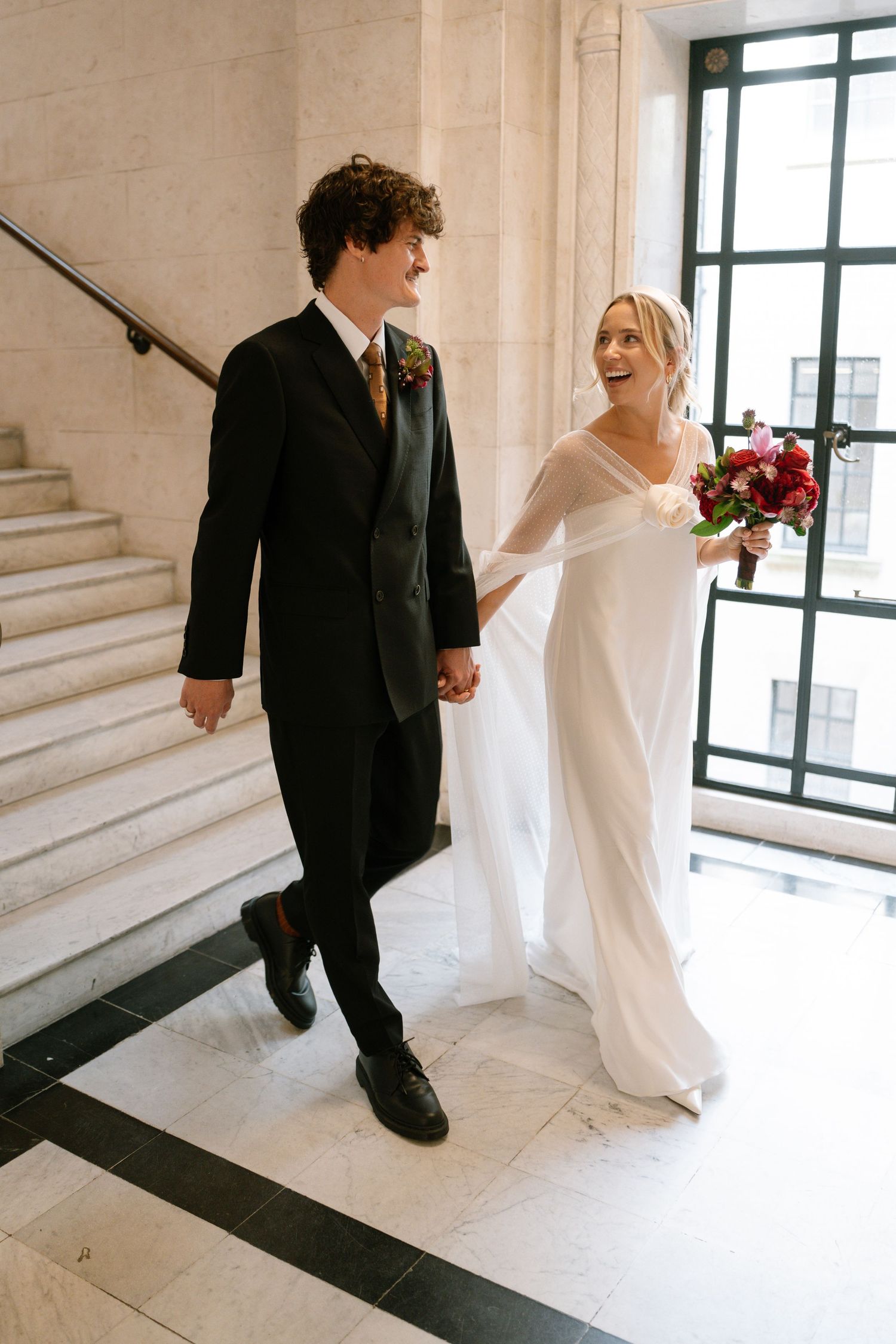 Wedding couple walking through a bright hallway with large windows, captured in a photo sequence.