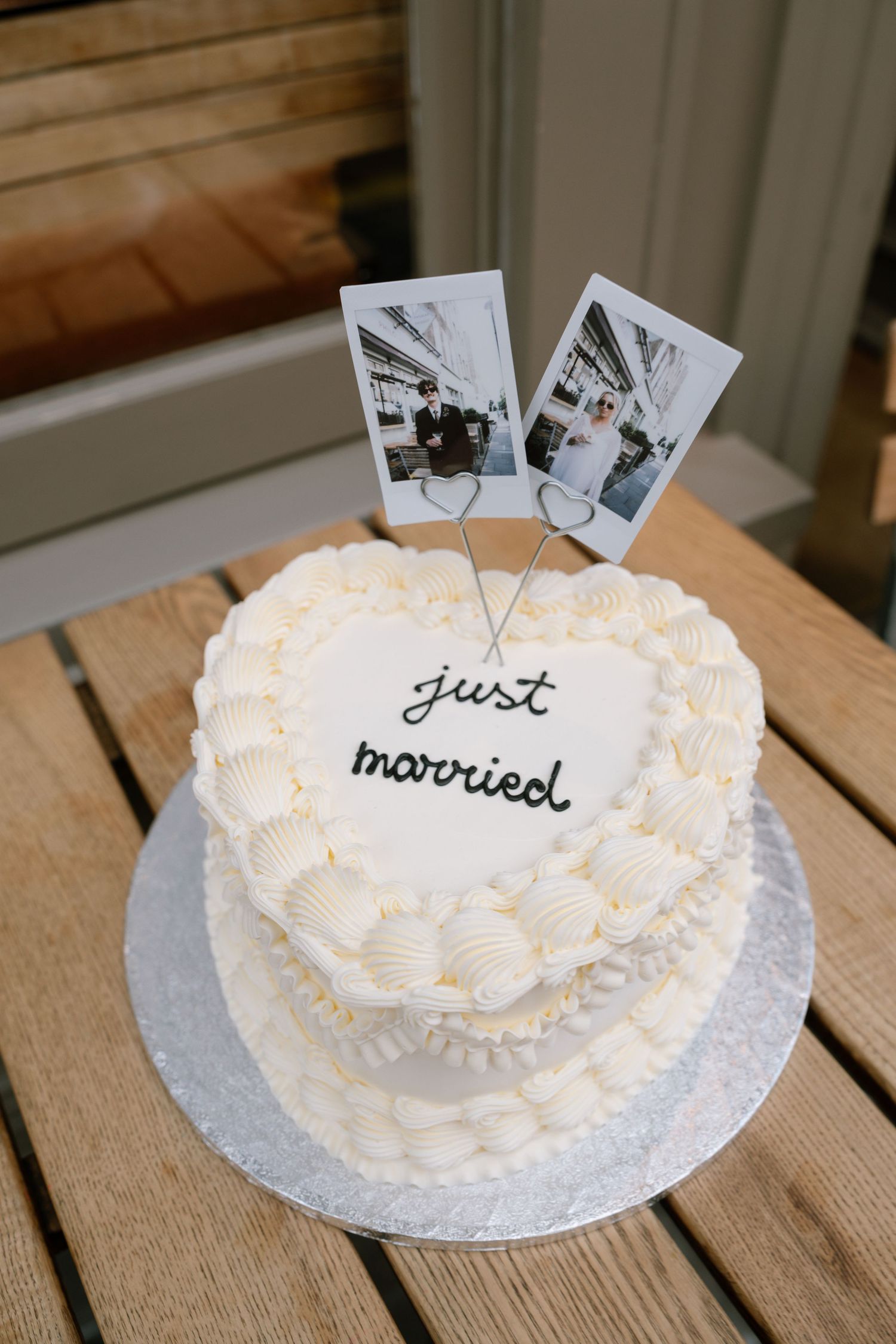 White heart-shaped wedding cake decorated with 'just married' text and black and white photos.