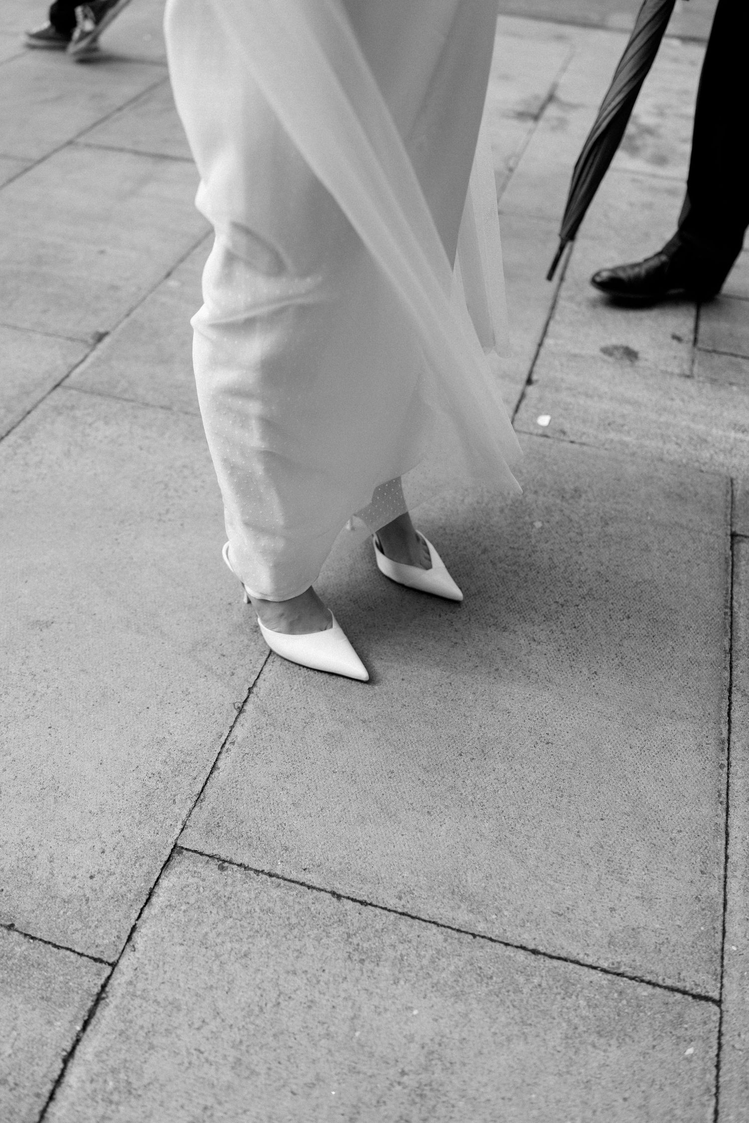 Close-up shots of white wedding dress and shoes moving across stone pavement.