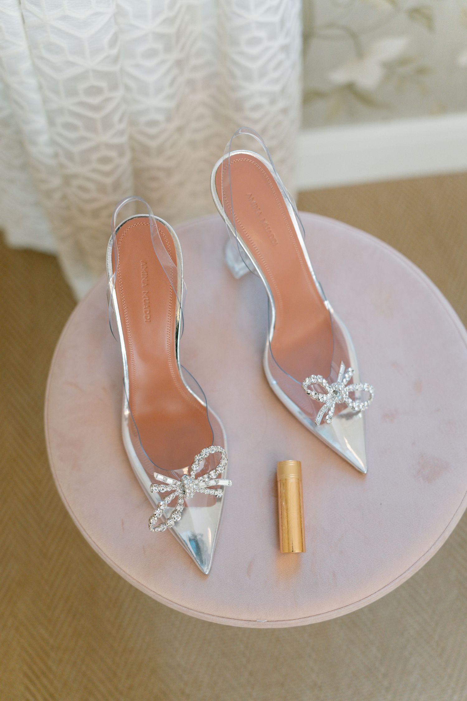 Elegant silver shoes and a metallic lipstick displayed on a pink surface.