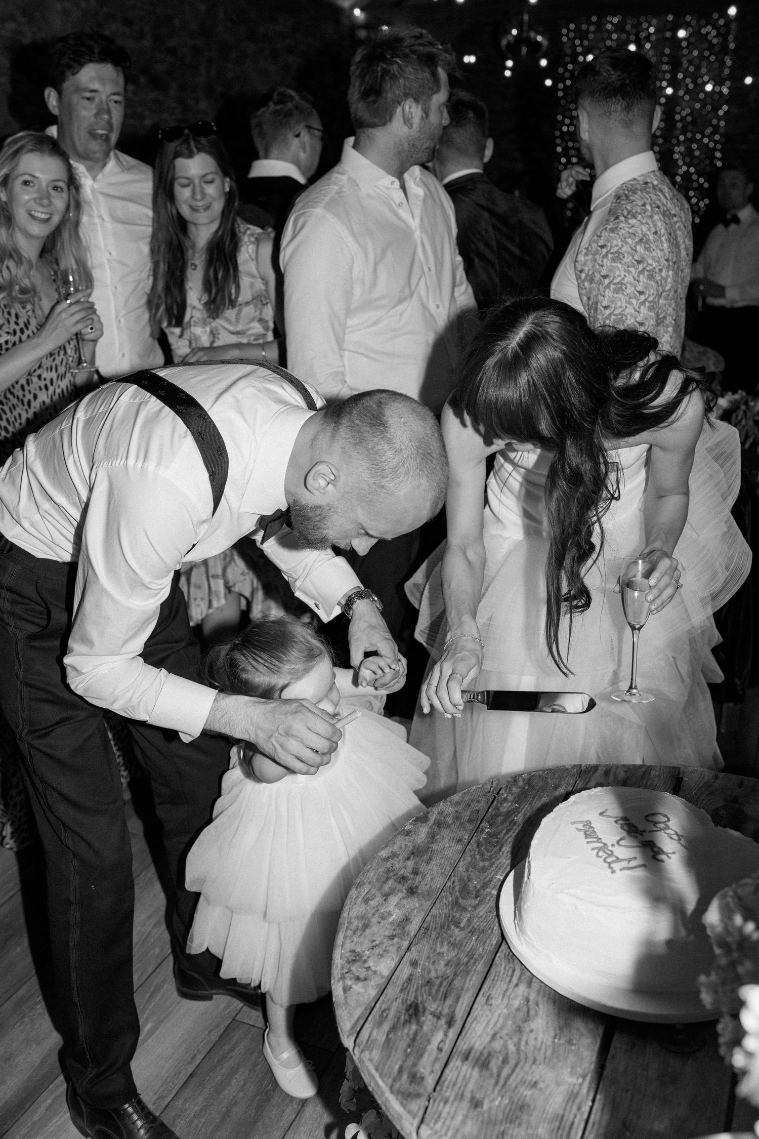 Wedding guests dance and celebrate at a reception under twinkling lights.
