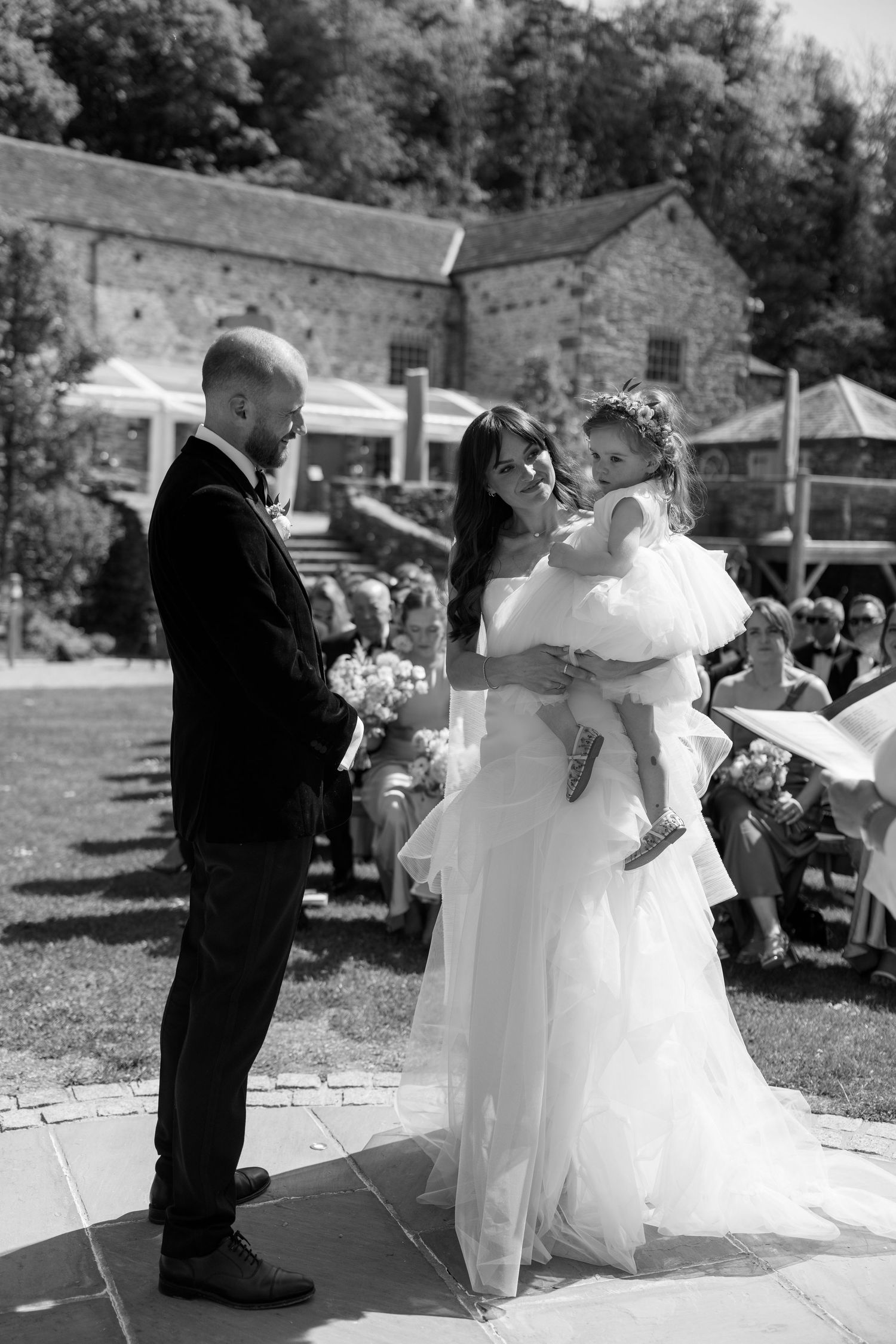 Wedding couple performs dance moves on stone patio during outdoor reception.