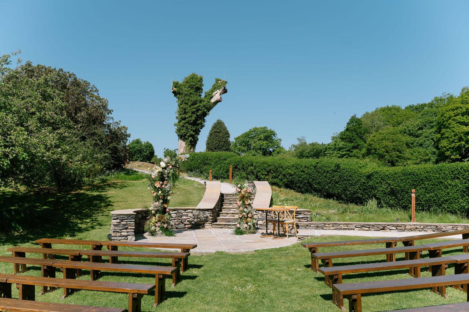 Panoramic view of an outdoor wedding venue with wooden pews and natural landscaping.