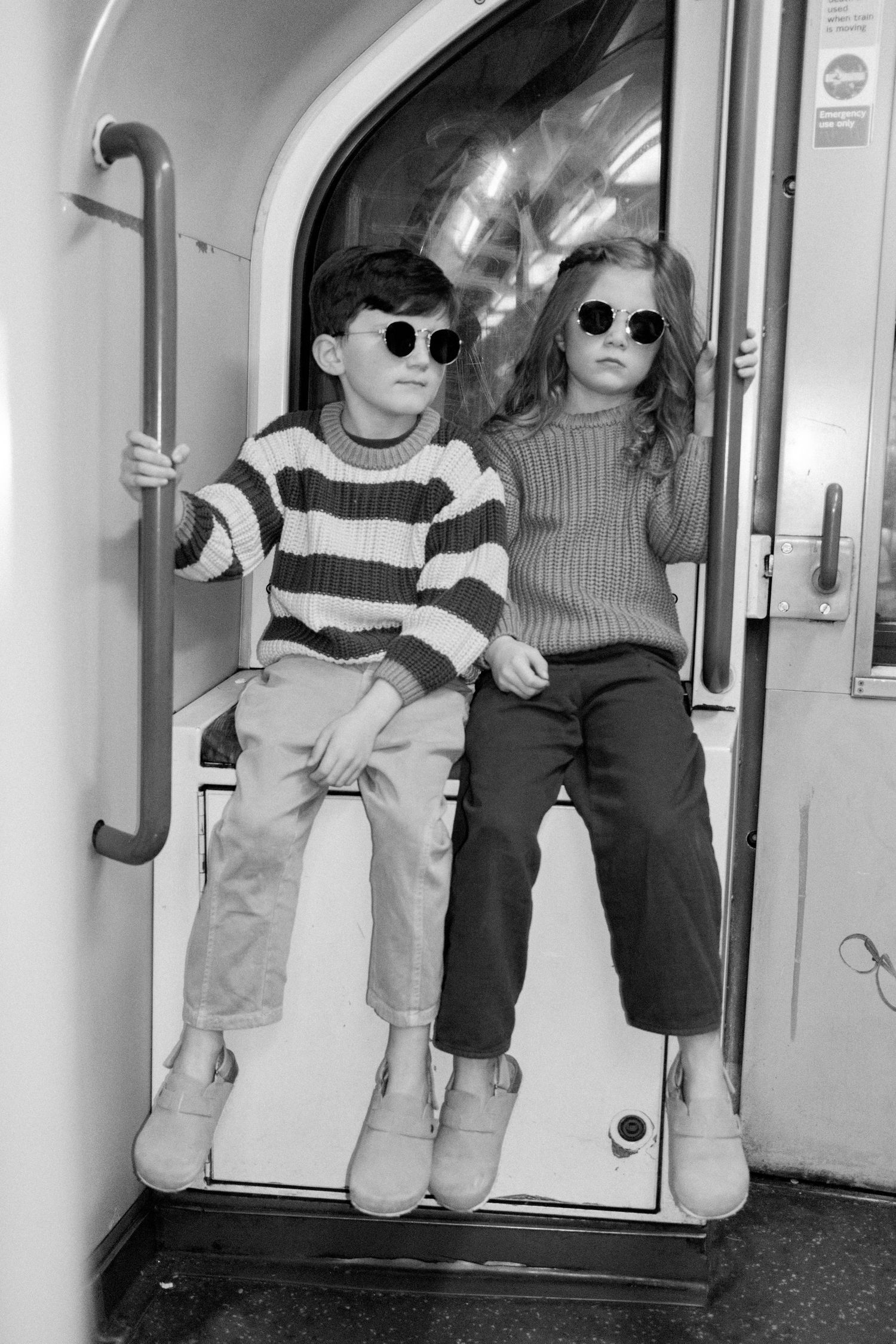 Children sitting on subway seats wearing matching outfits and sunglasses.