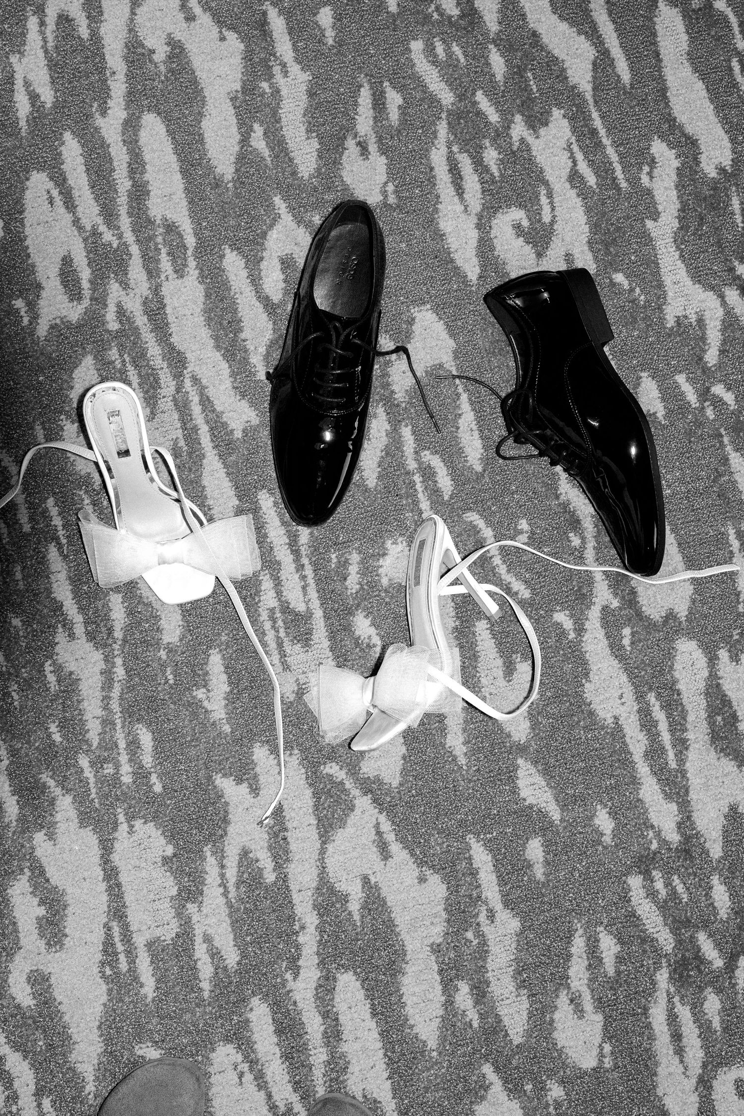 Black and white image of shoes and shadows on textured surface.