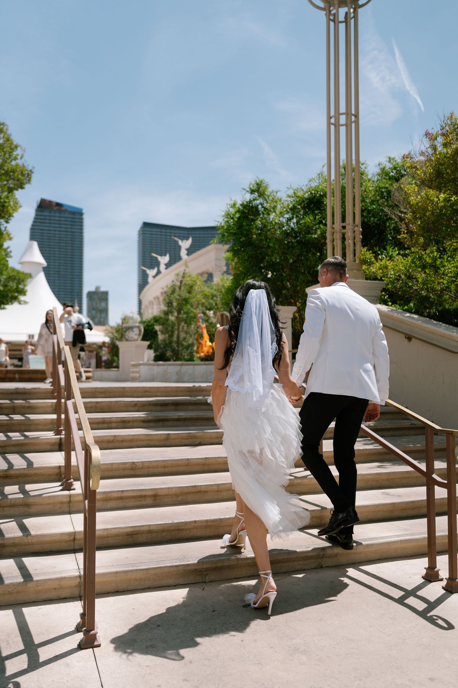 A wedding couple climbs outdoor stairs with Las Vegas architecture in the background.