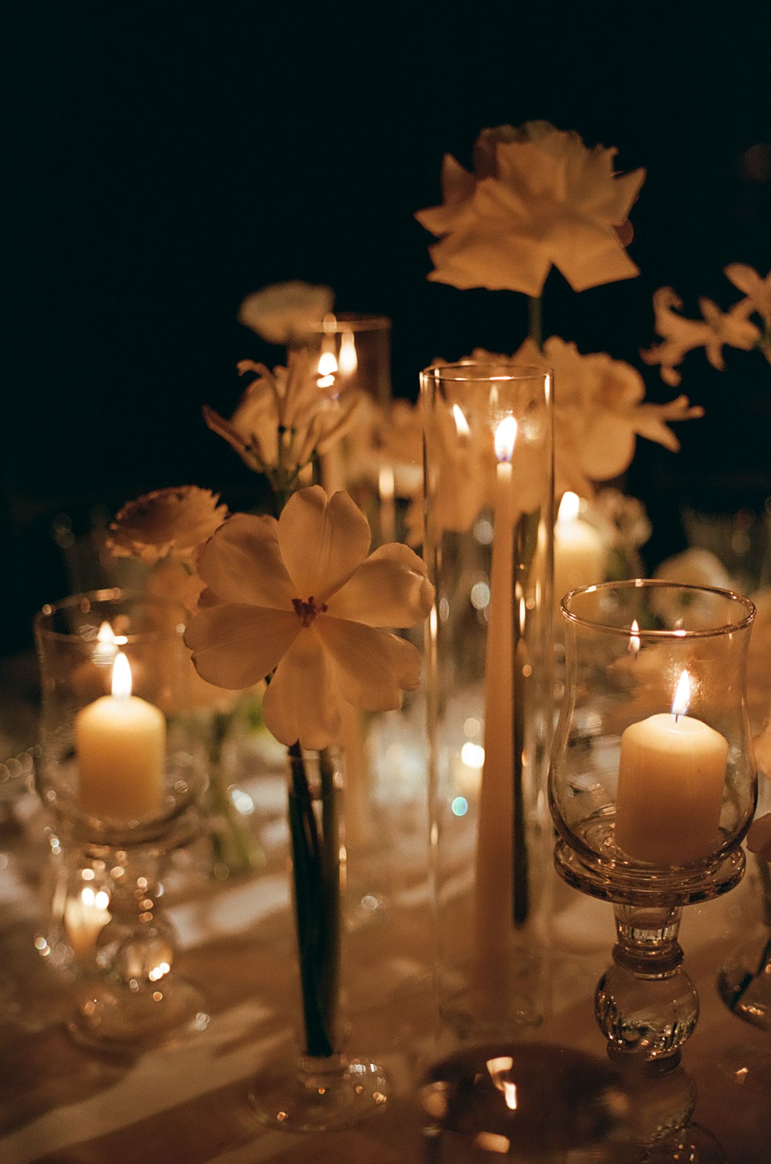 Romantic candlelit table setting with white flowers and glass votives creating a soft ambiance.