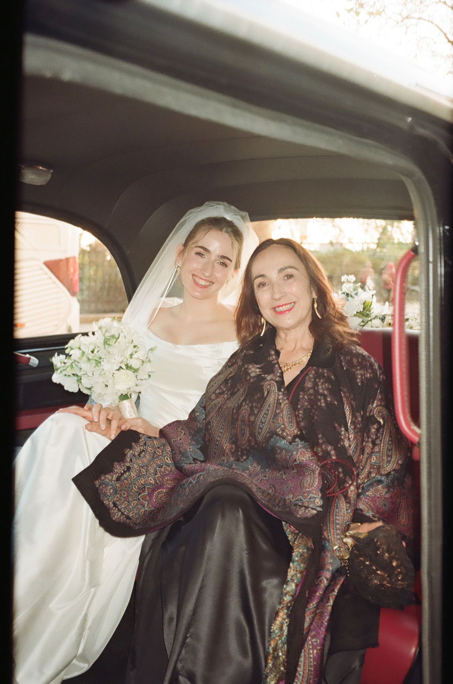 People share a joyful moment while sitting in a classic red car interior.