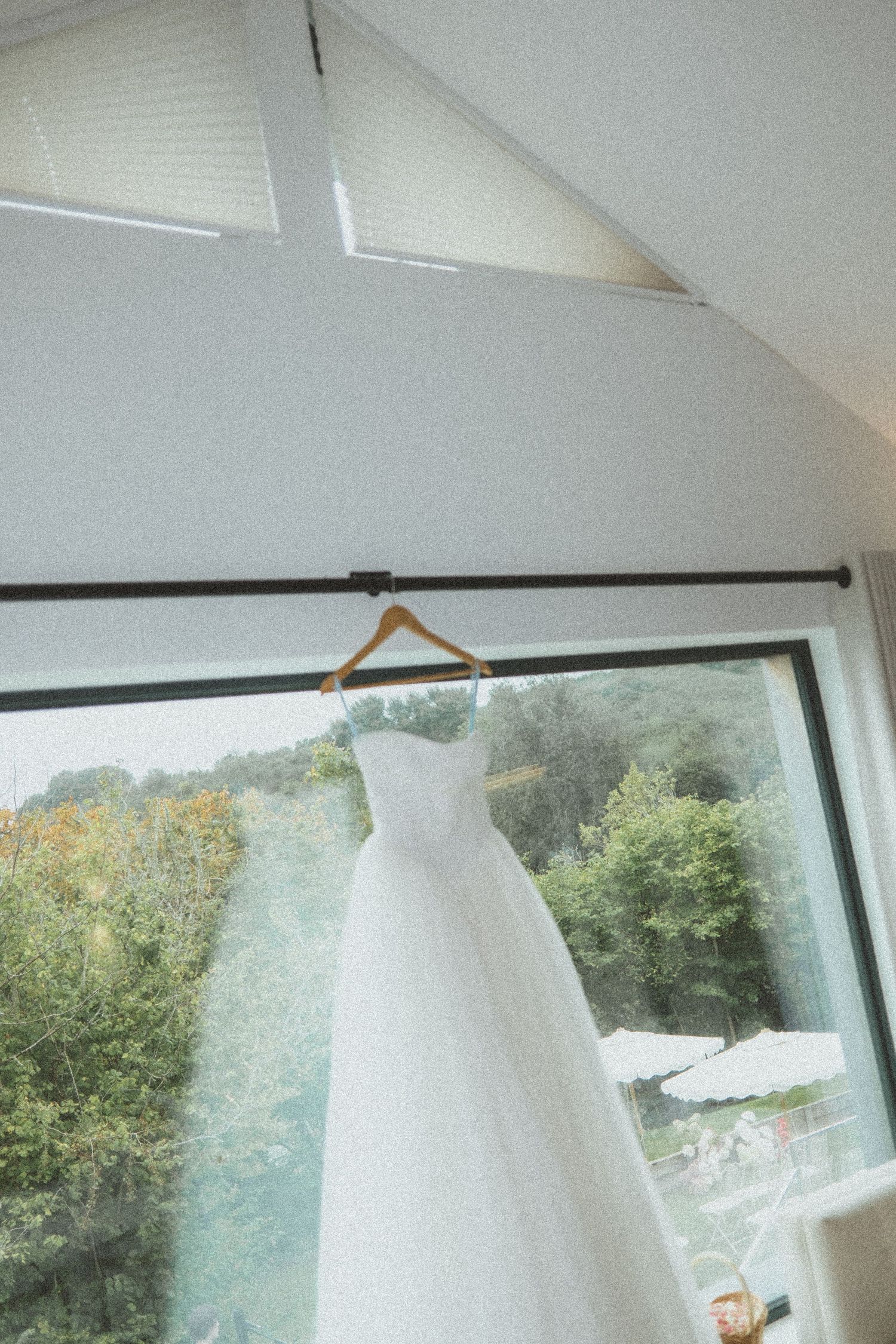 A row of white pendant lights hang from a sloped ceiling with large windows overlooking green trees outside.