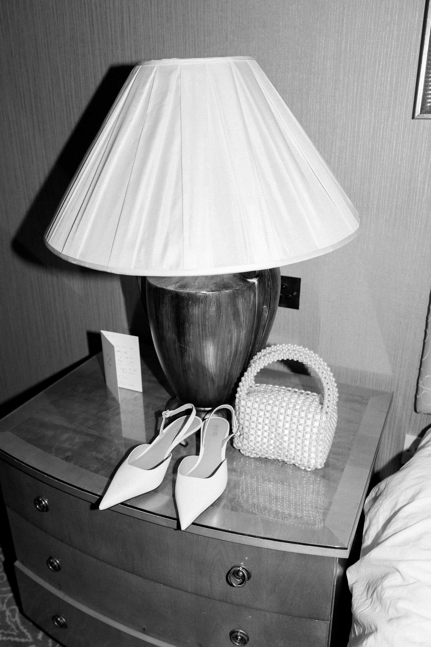 Black and white photo series showing a table lamp with white shade and two decorative white shoes on a dark wooden surface.