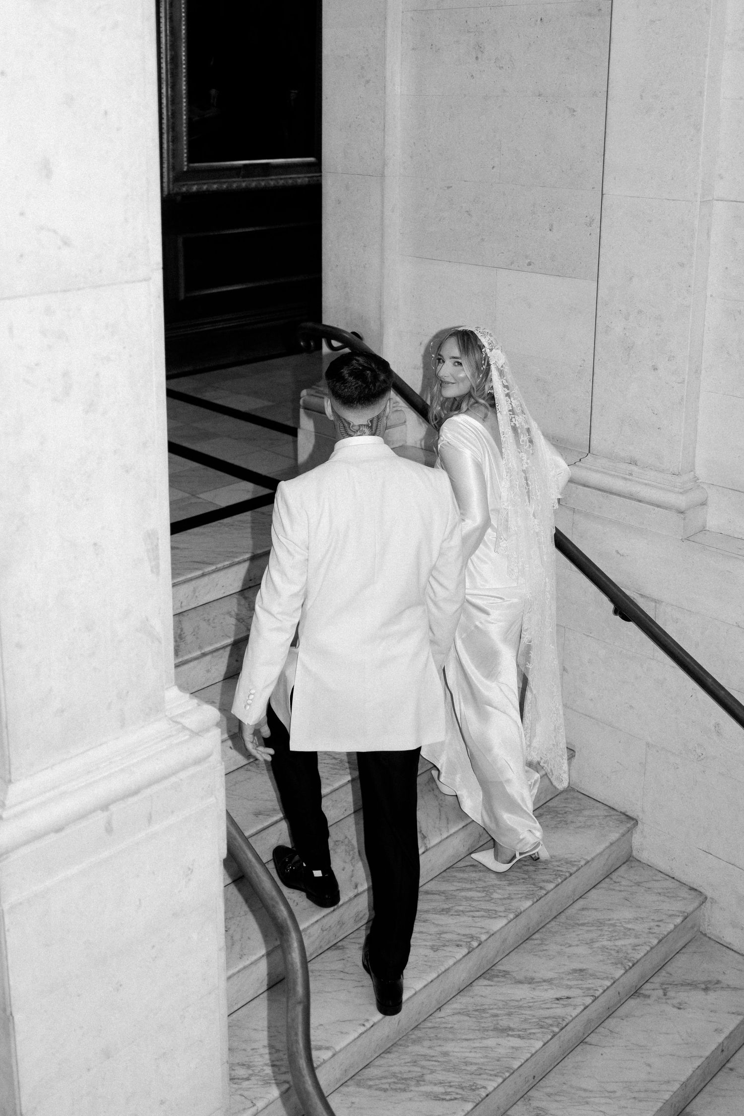 A black and white photo of newlyweds dancing in an elegant hallway.