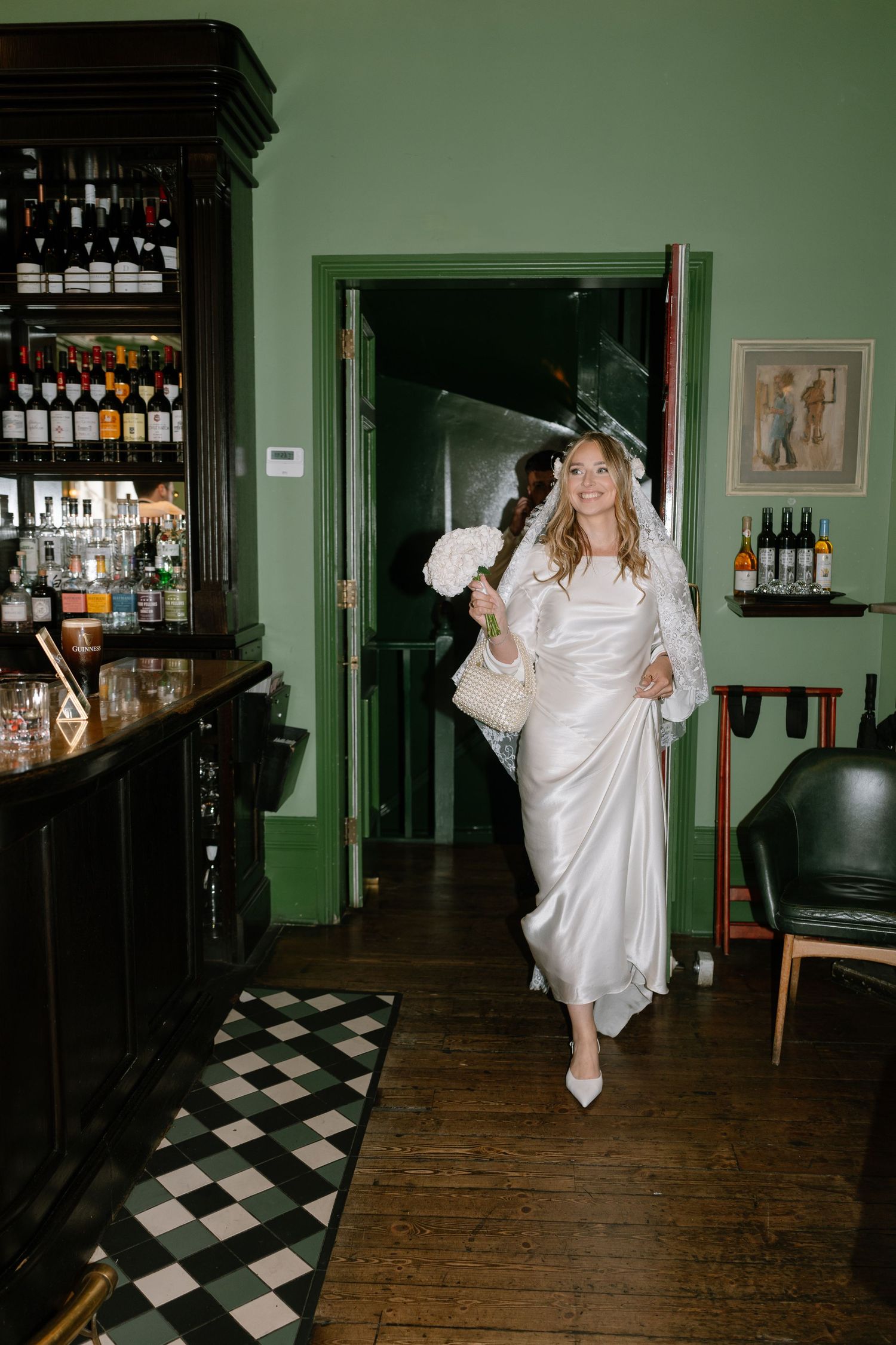 Person in white dress dancing in a bar area with checkered floor and green walls.