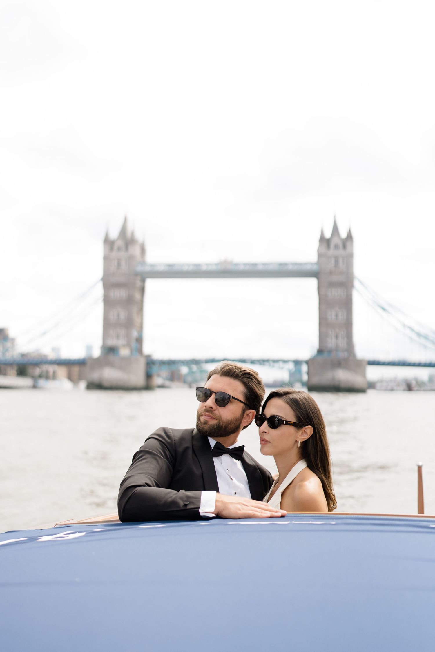 A couple shares a romantic moment on a boat with London's iconic Tower Bridge in the background.