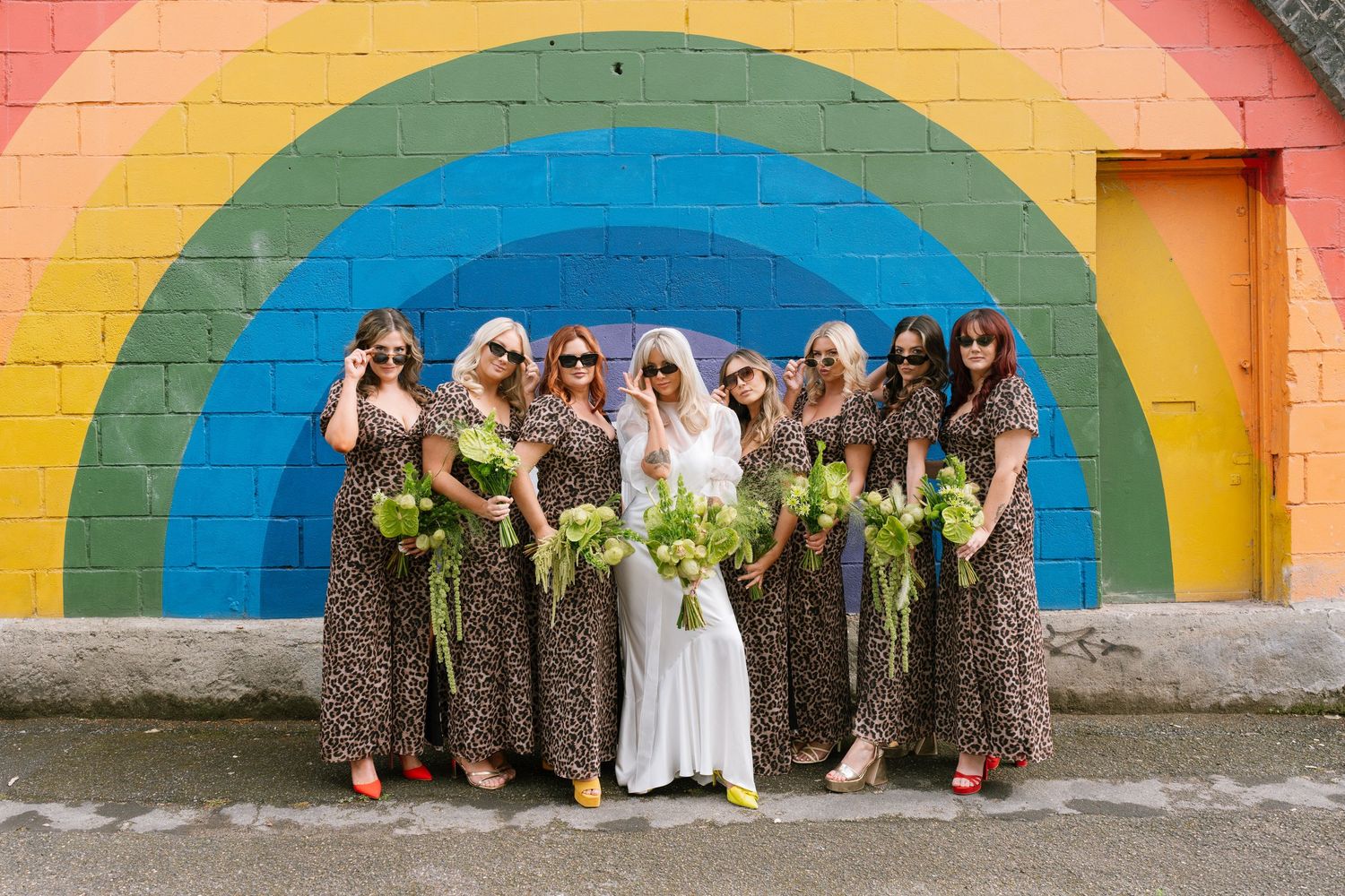 Wedding group photo against vibrant rainbow painted wall mural outdoors.