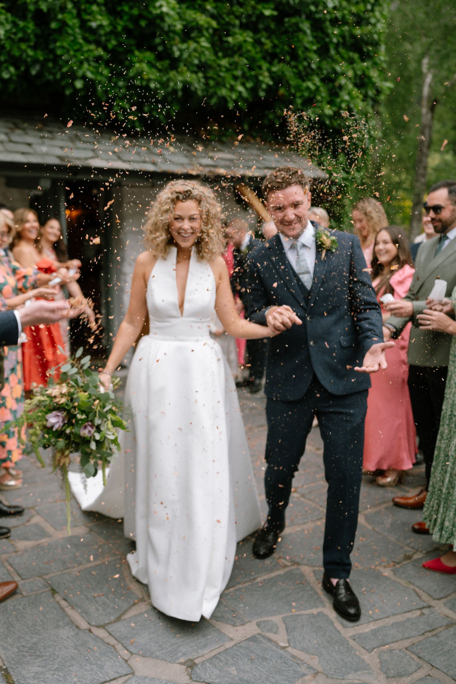 Newlyweds walk down a path while guests throw confetti in celebration.