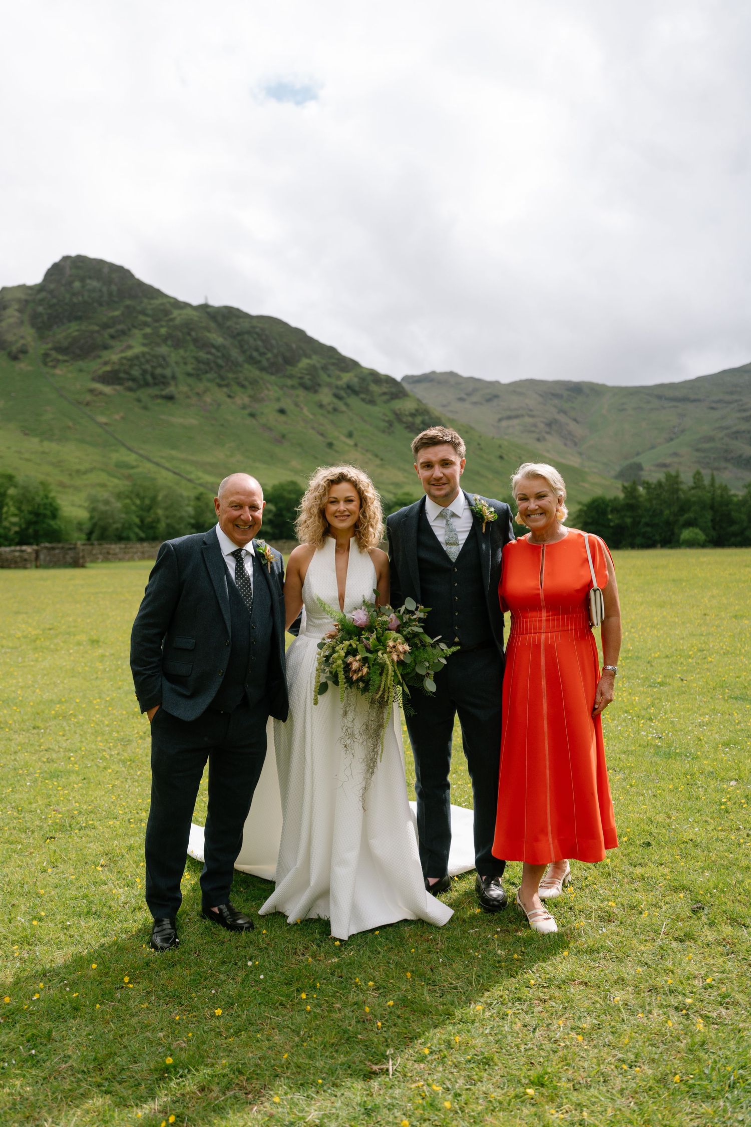 A wedding party poses in a lush green field with mountains in the background.