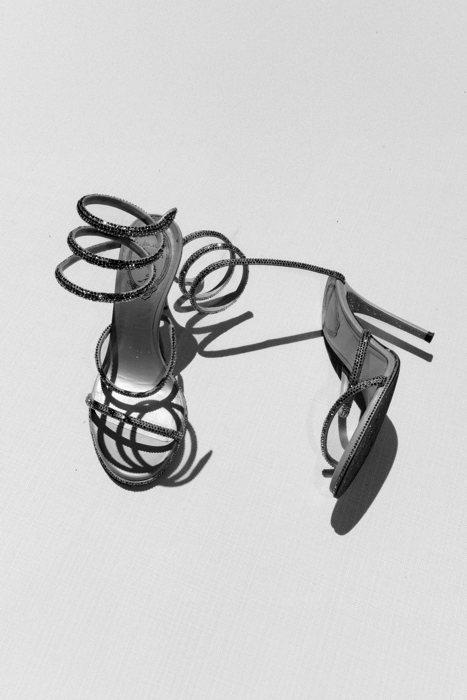 Artistic still life composition of black strappy high heel shoes against a white background.