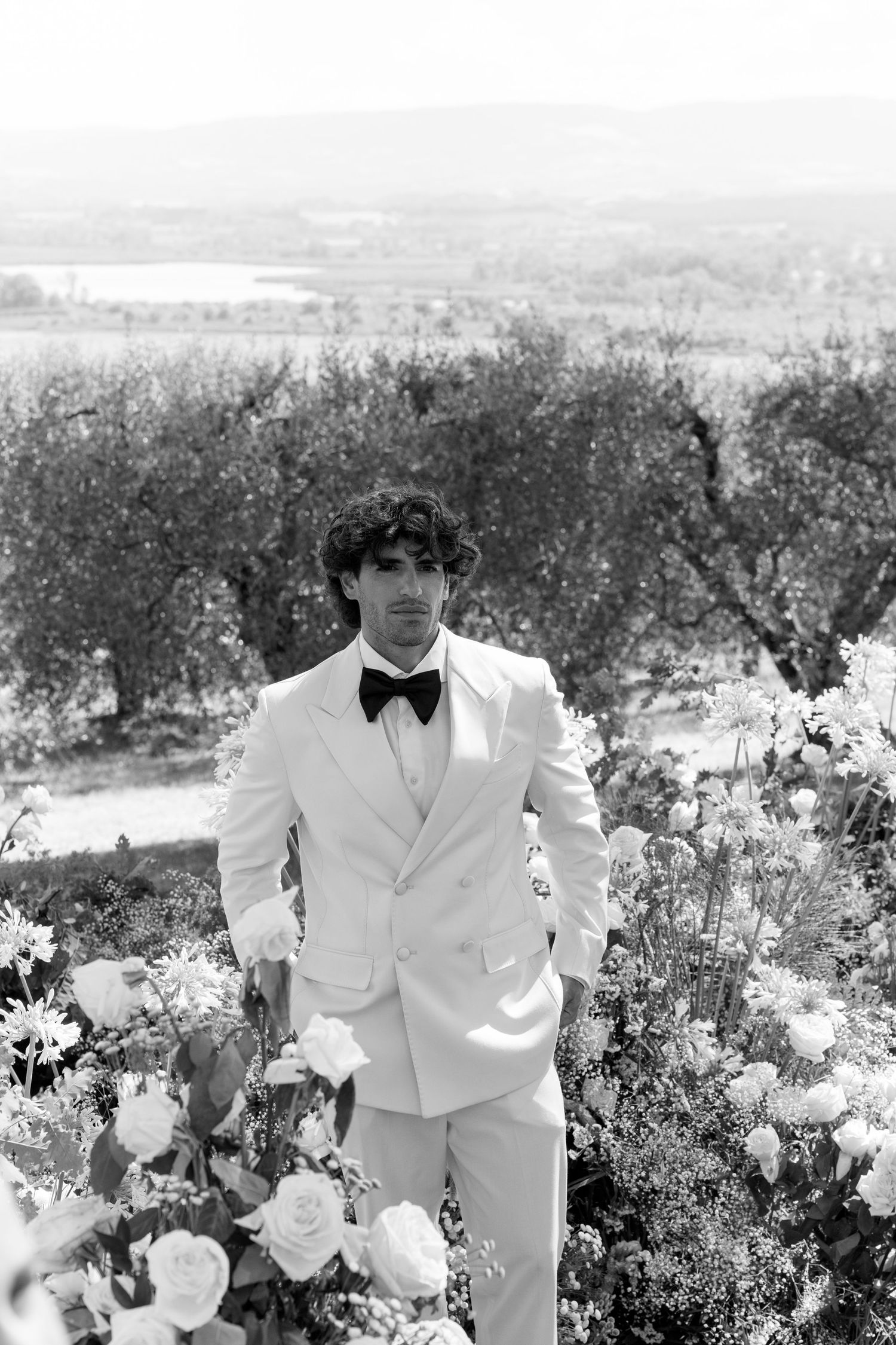 White roses and floral arrangements frame a scenic outdoor wedding setting in black and white.