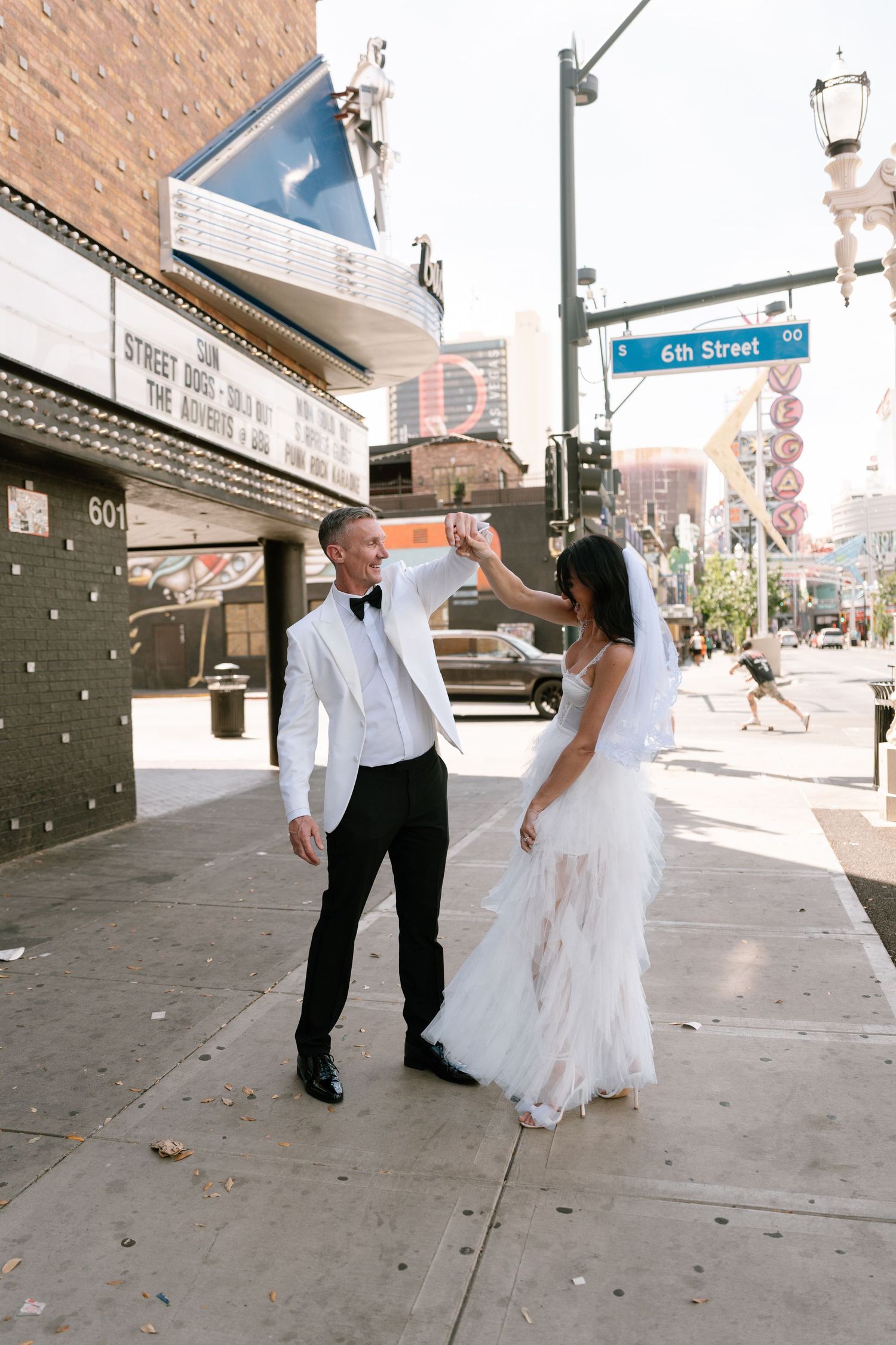 A couple in wedding attire dancing and twirling on a city sidewalk.