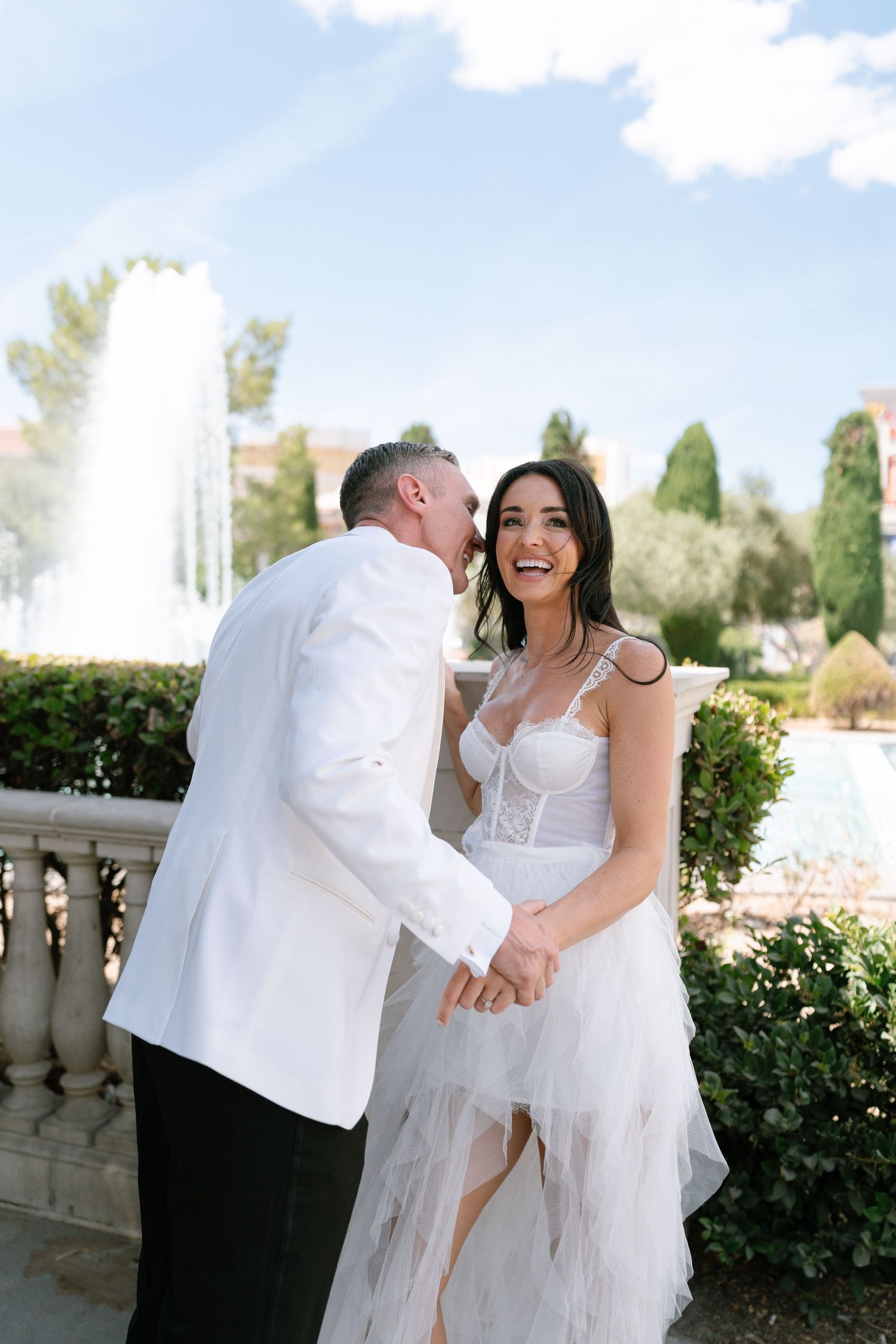 Wedding couple shares joyful moment by fountain at luxury resort.