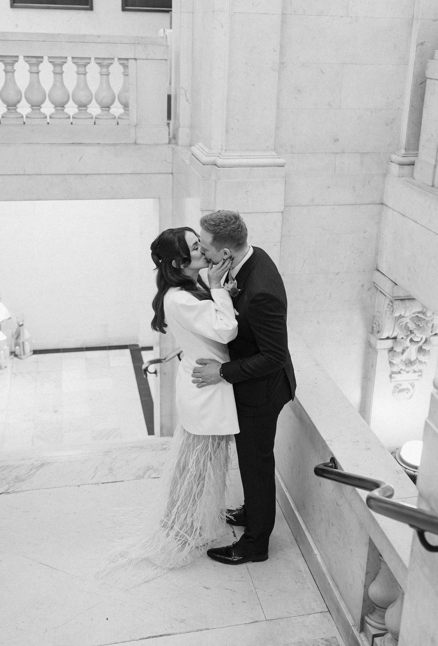 Bride and groom share first kiss on marble staircase in black and white wedding photo.