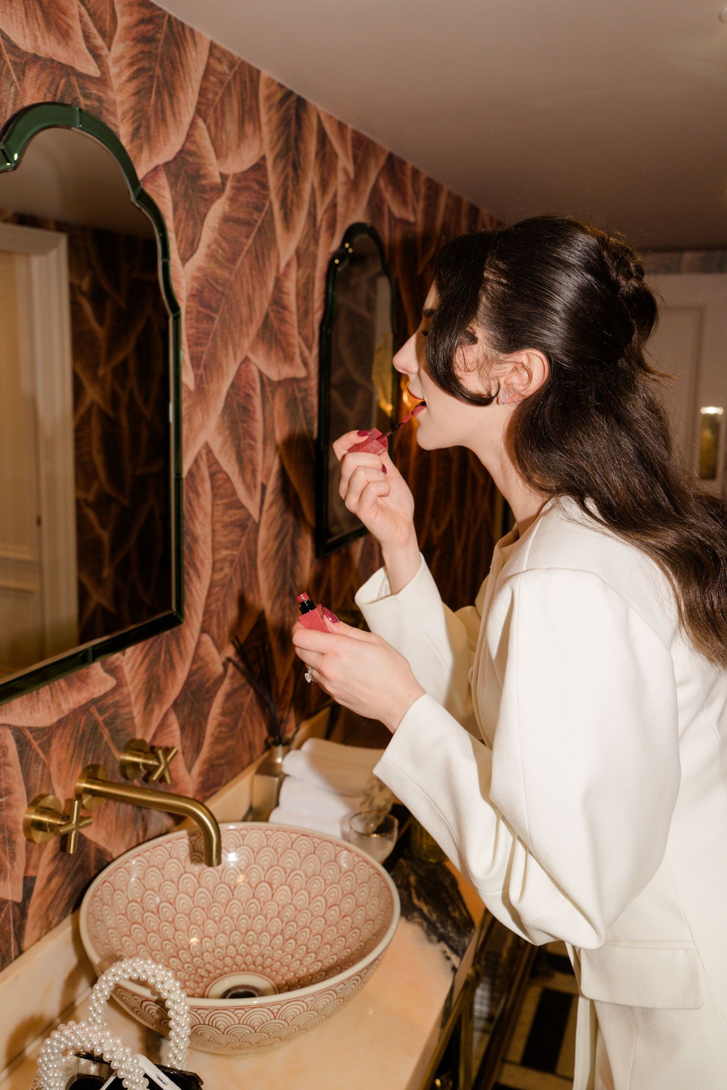 Bride applying lipstick in a stylish bathroom mirror before her wedding ceremony.