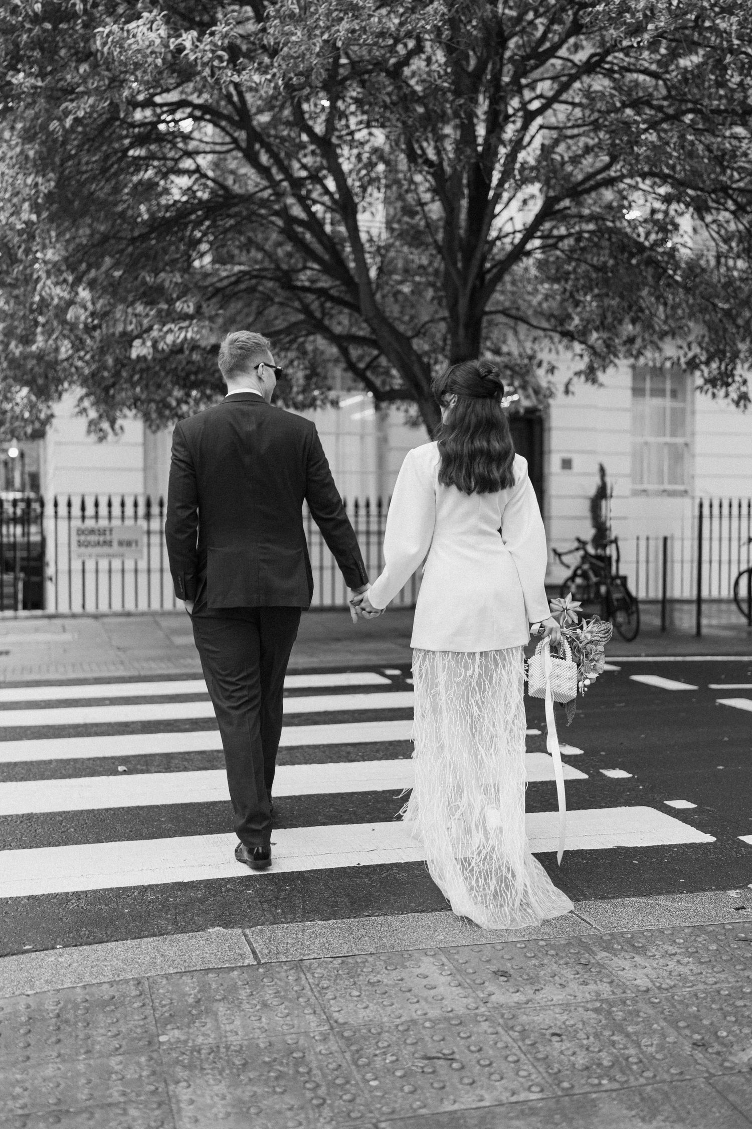 Newlywed couple holding hands crossing a zebra crossing on their wedding day.