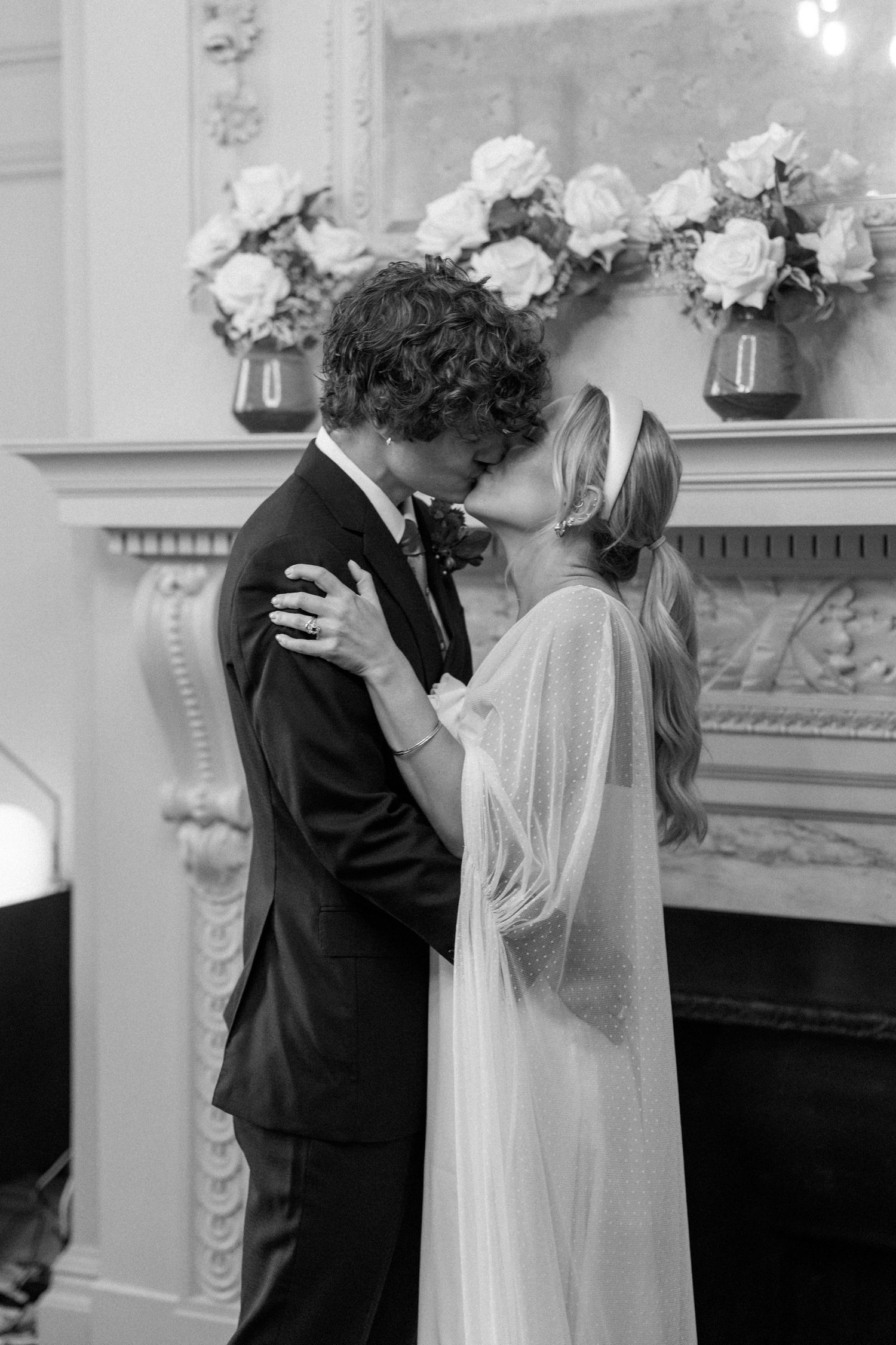 Black and white wedding photos capturing intimate moments between a couple by an ornate fireplace.