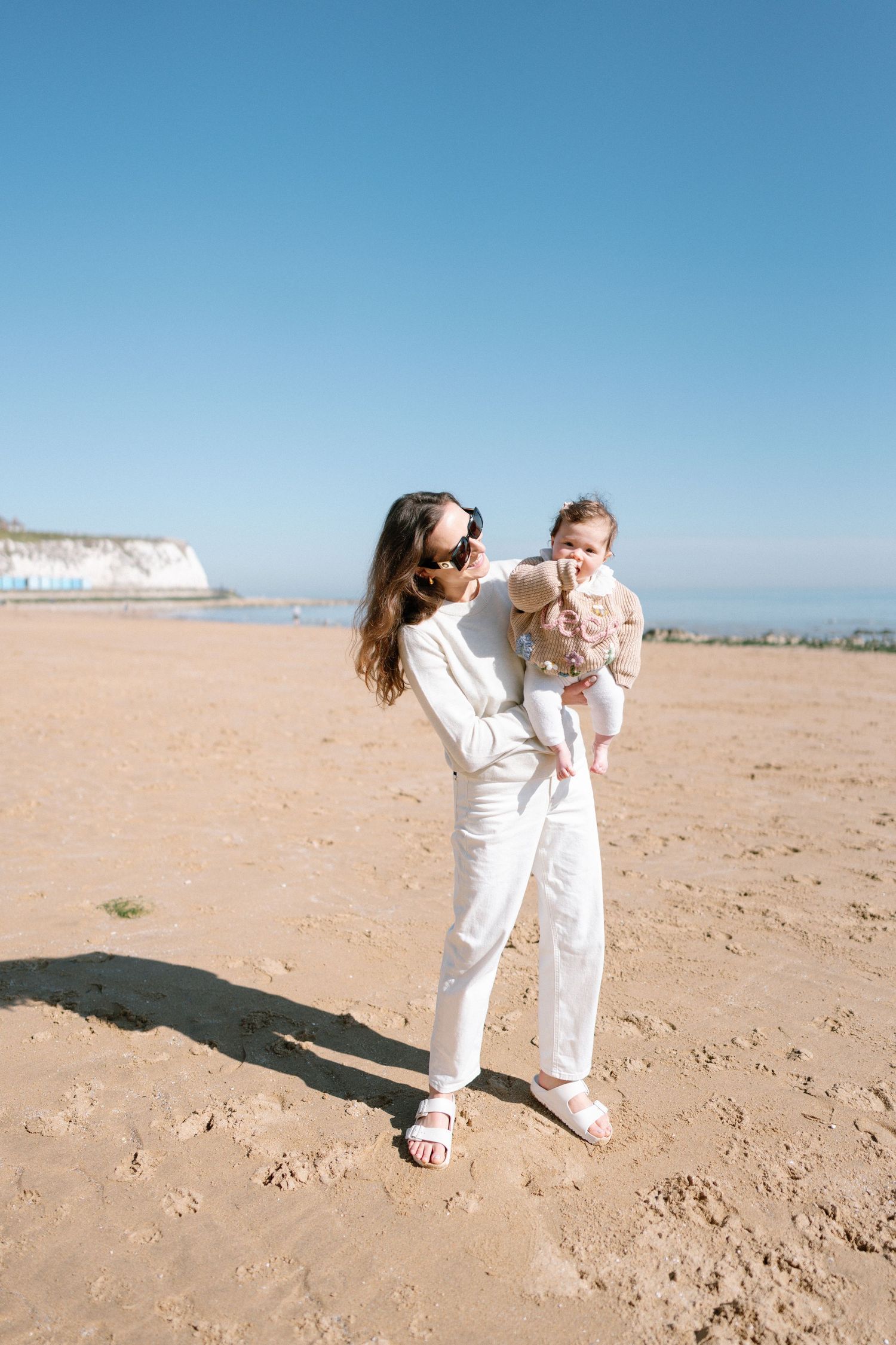 Family in coordinated white outfits playing together on a sandy beach under blue skies.
