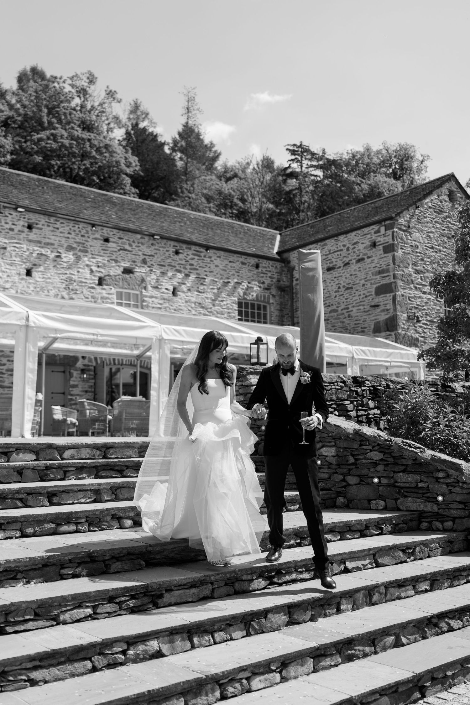 Wedding couple descending stone amphitheater steps under a white canopy.