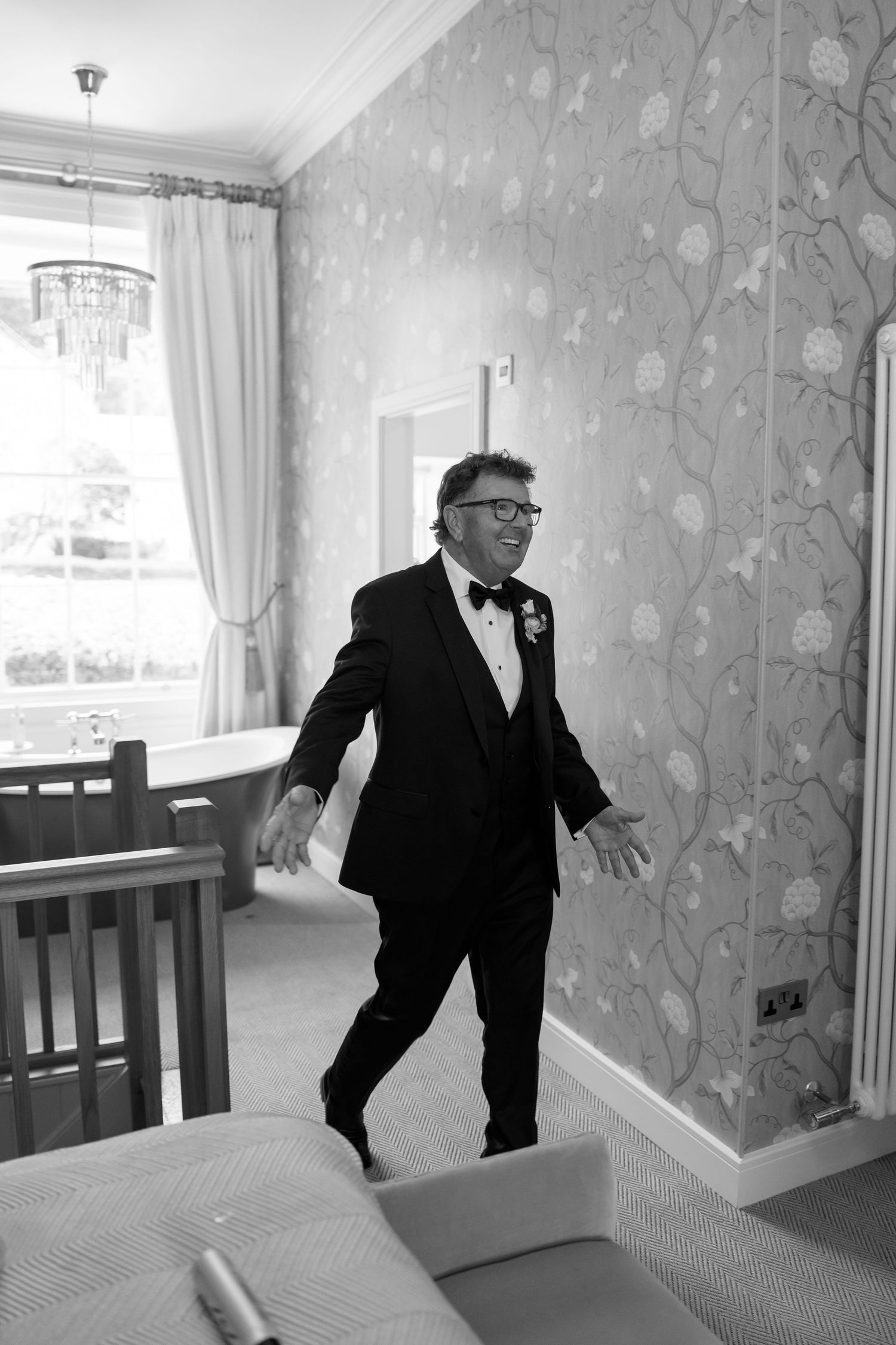 A candid moment showing someone in a tuxedo gesturing with their arms in a decorated room.