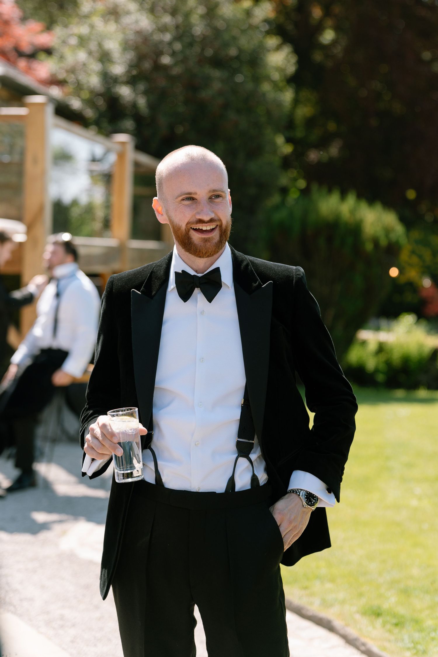 Men in black tuxedos and bow ties enjoying a sunny outdoor celebration.