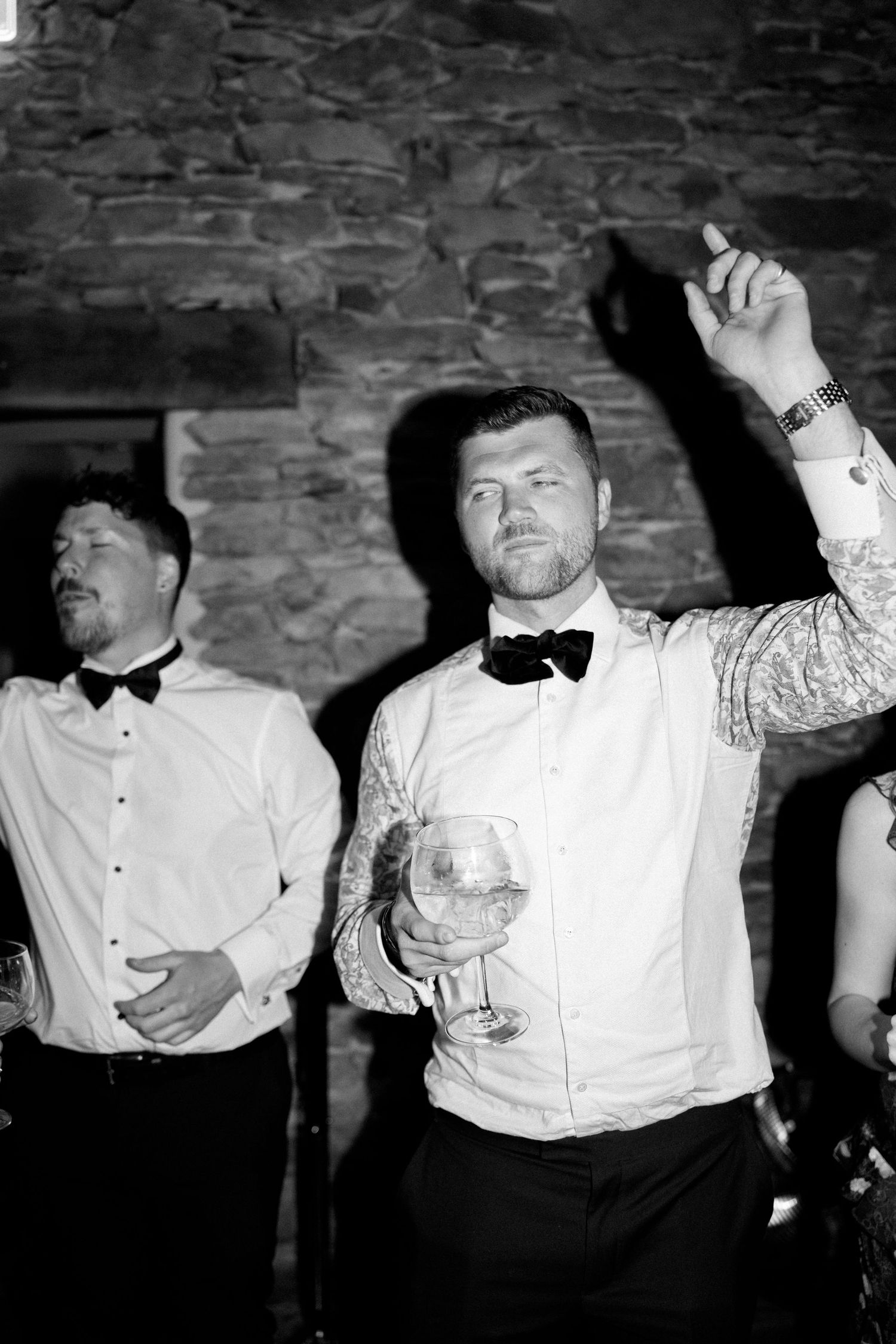 Black and white shot of guests in formal attire dancing enthusiastically at an event.