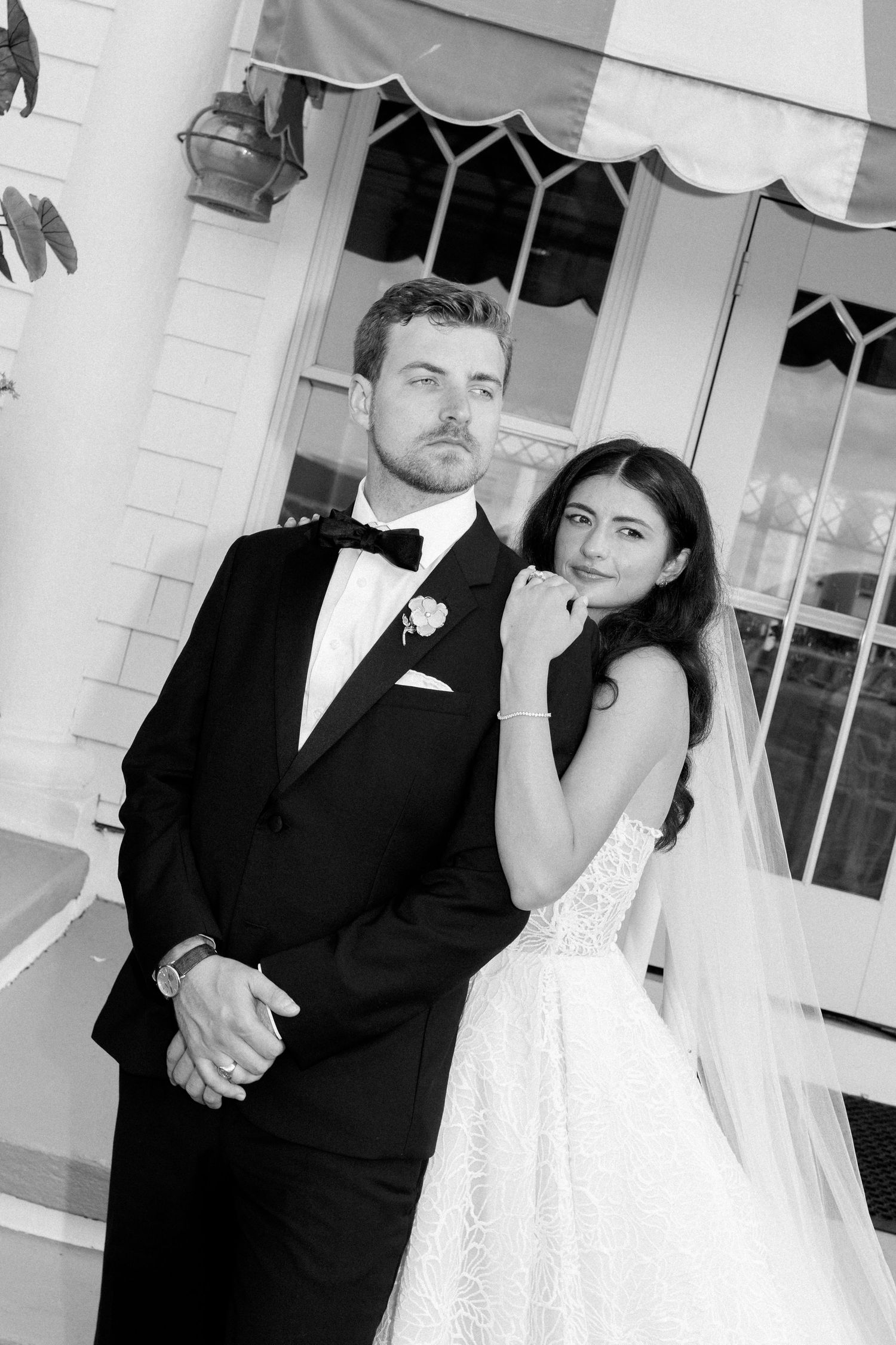 Black and white wedding portrait of bride and groom posing elegantly outside a classic venue.