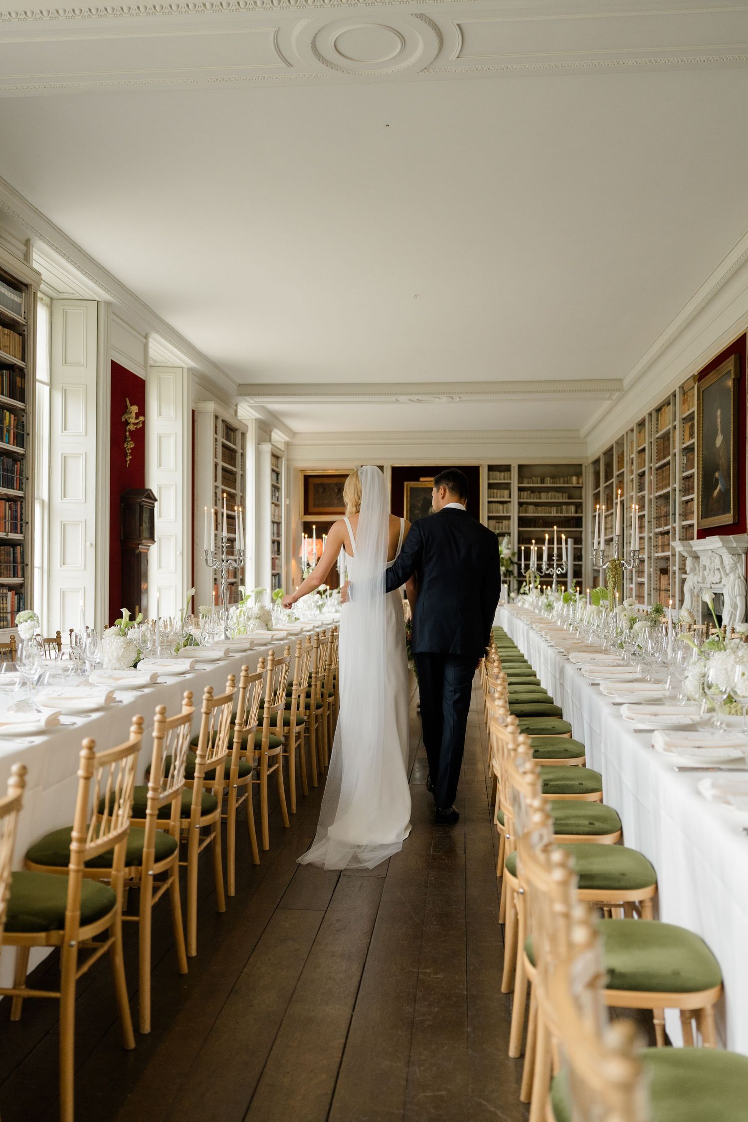 Bride and groom walk between long reception tables in a stunning library wedding venue.