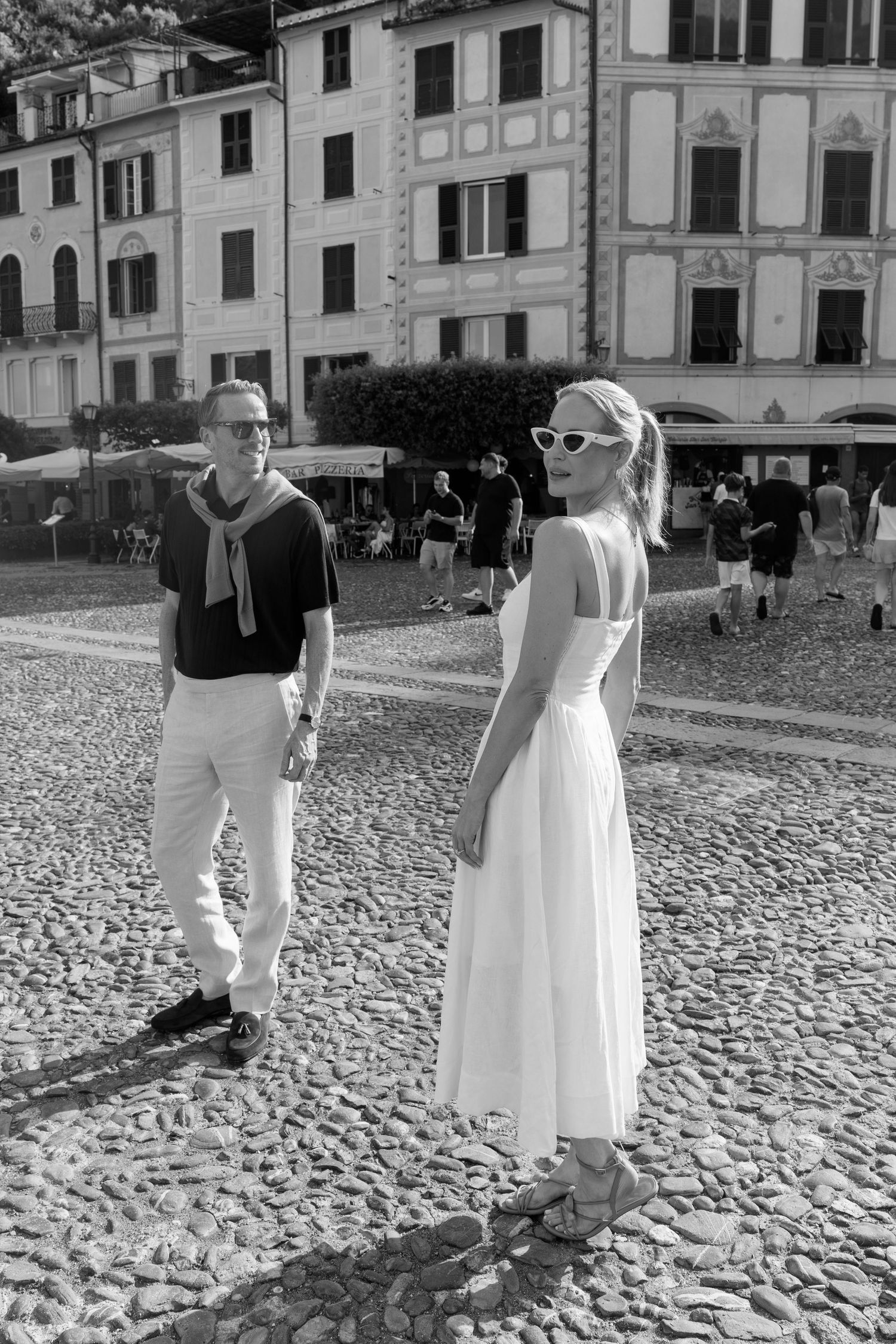 Black and white photo of stylish couple holding hands on cobblestone piazza in Portofino, Italy.
