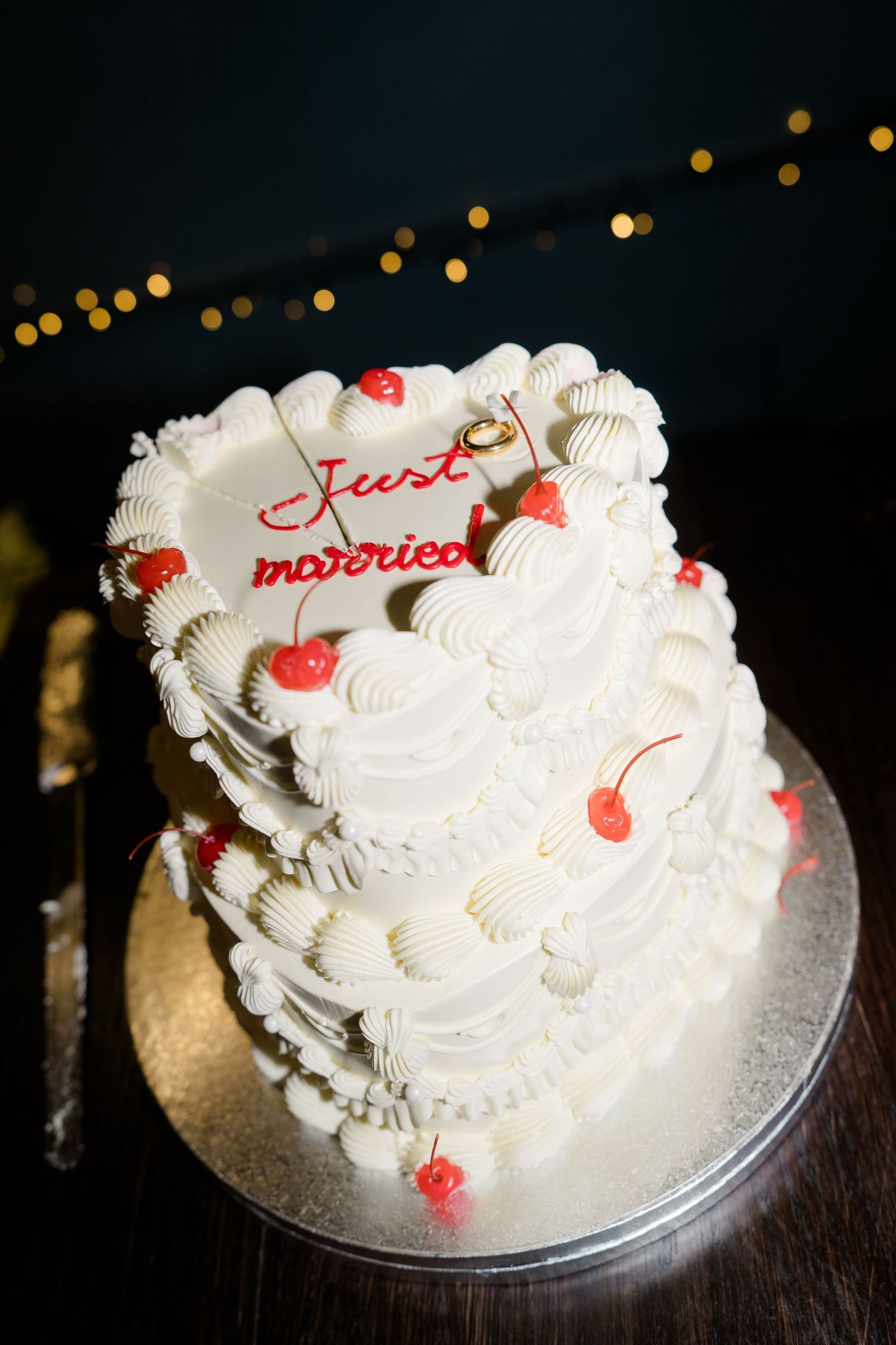 White heart-shaped wedding cake with red cherries and Just Married topper.