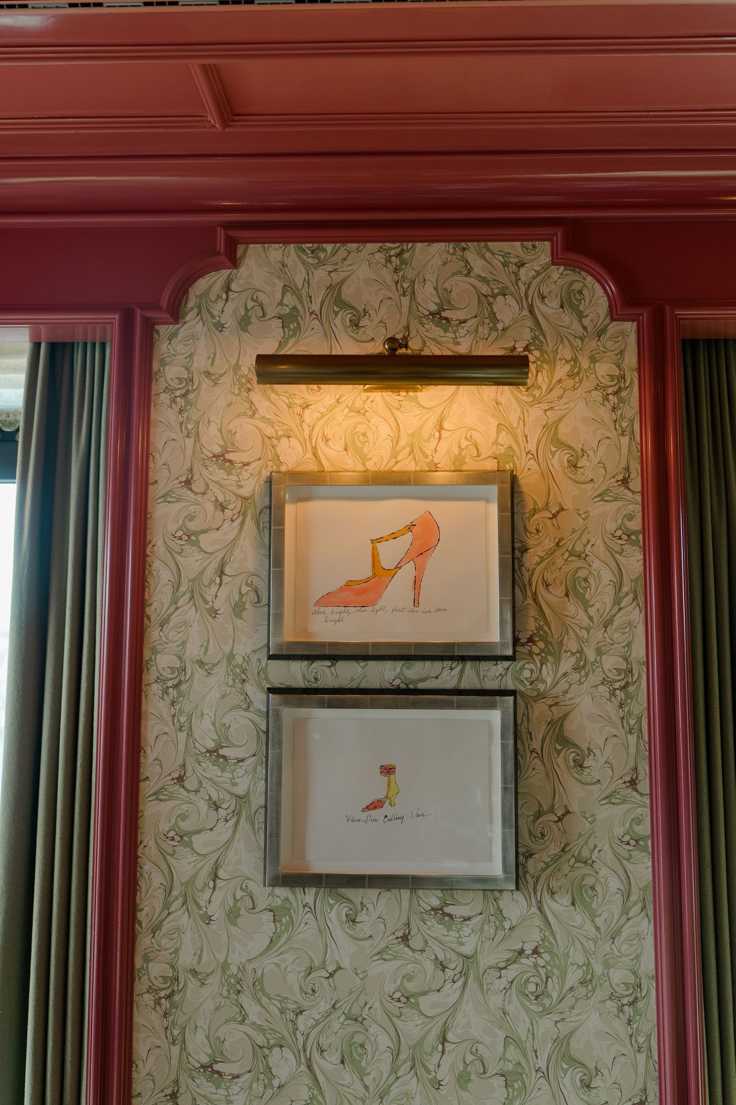 Two framed watercolor illustrations of elegant high heel shoes displayed on ornate wallpapered wall.