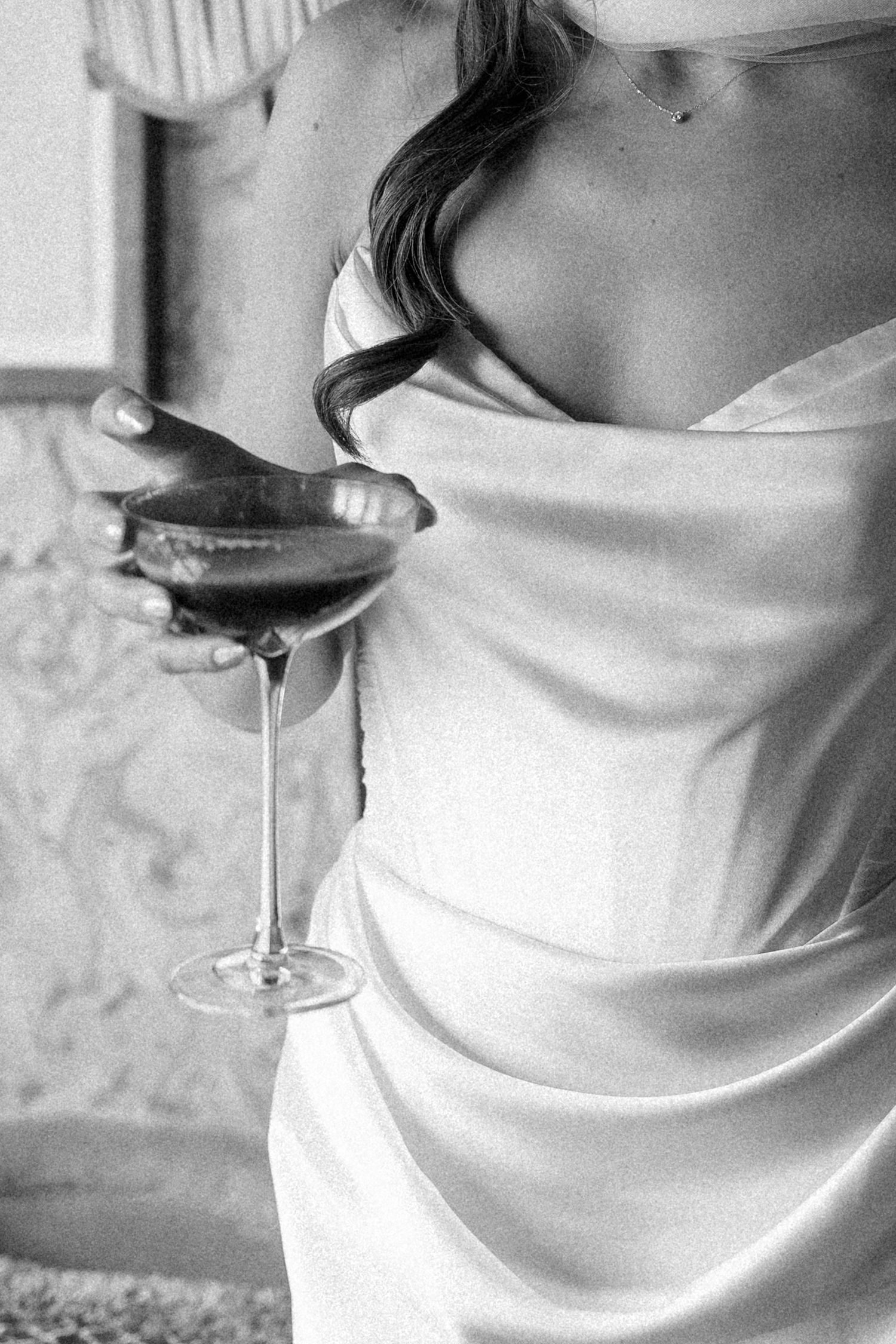 Black and white close-up of bride in satin dress holding a cocktail glass at wedding reception.