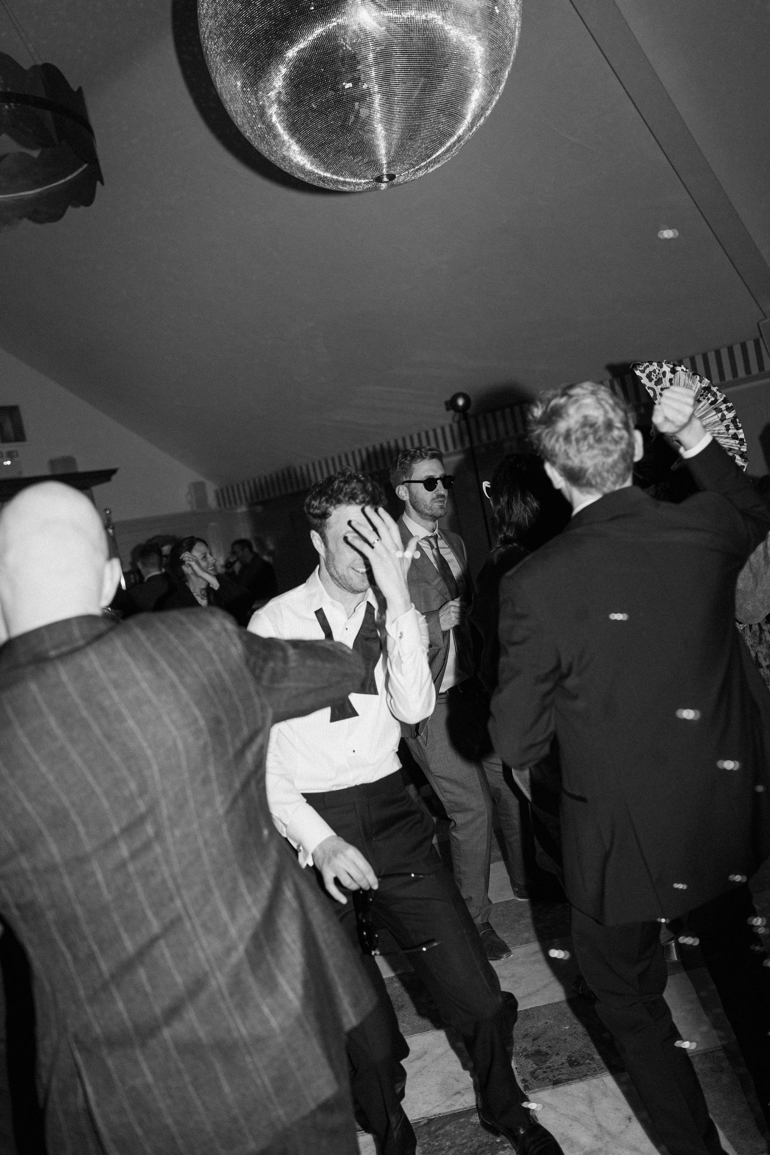 Guests dance energetically under a glittering disco ball at a lively wedding reception party.