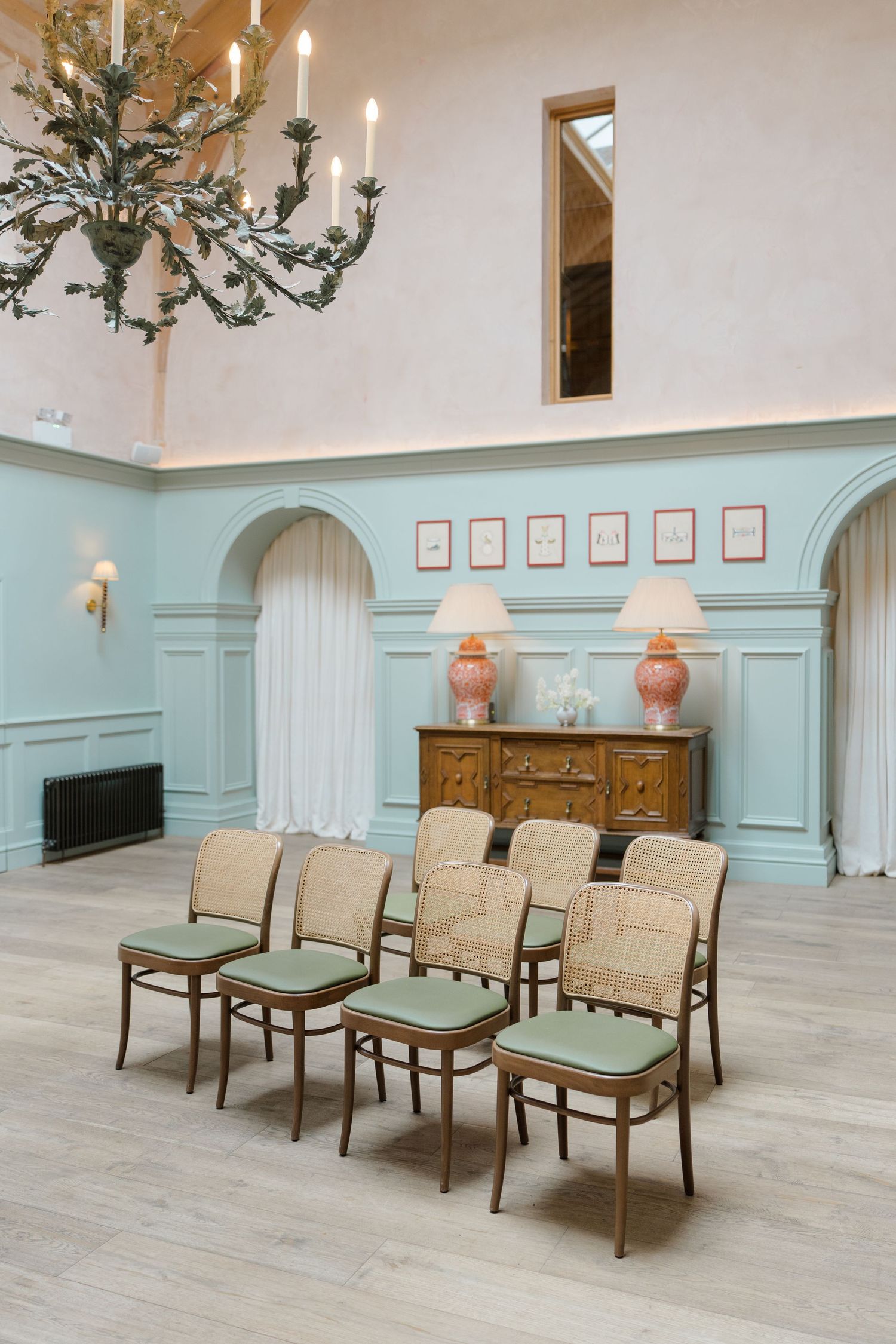 Elegant wedding ceremony room with mint green walls, cane chairs with sage cushions, and ornate chandelier.