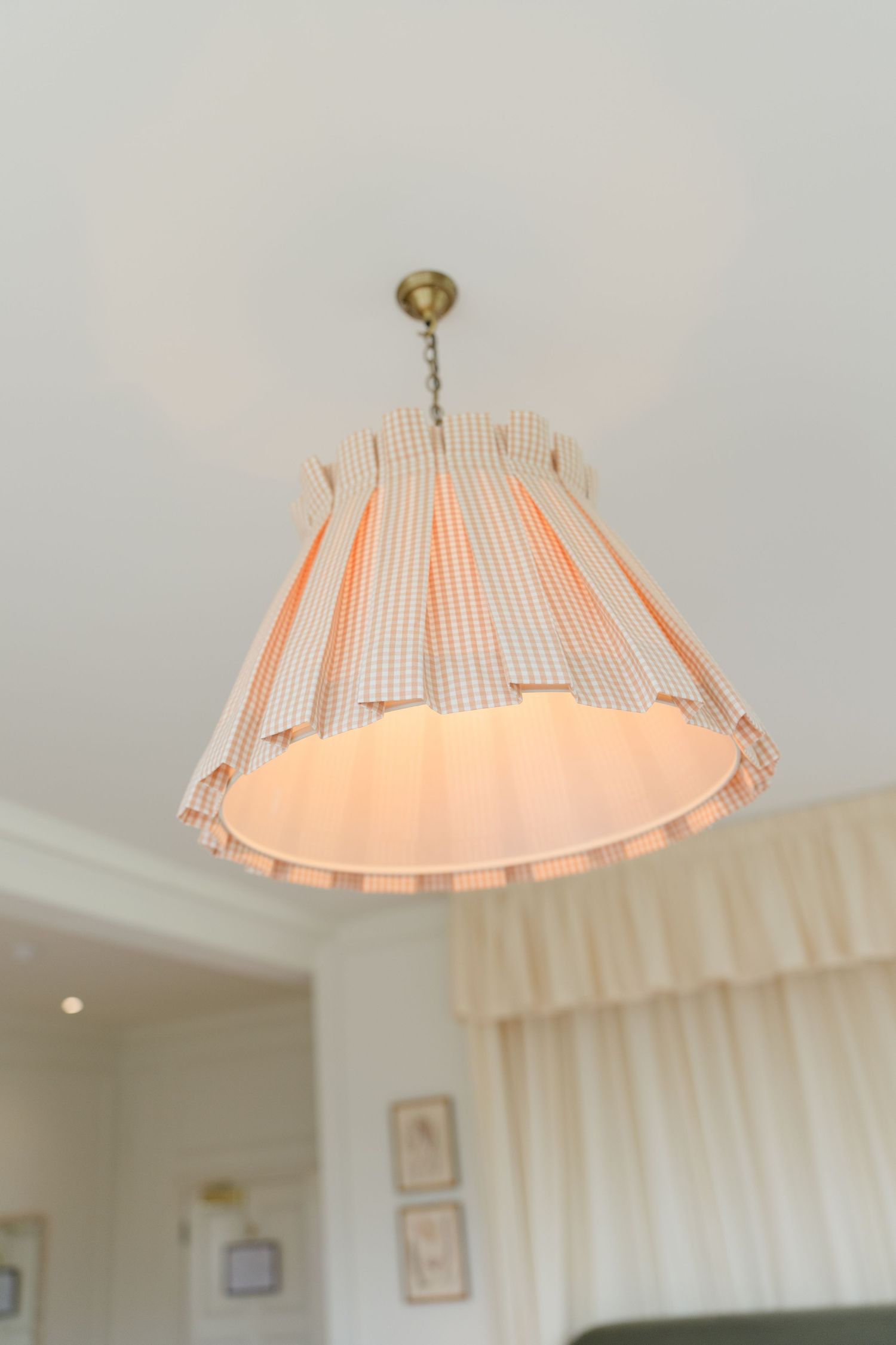 Decorative pleated fabric pendant light with orange trim hanging from a white ceiling in an elegant room.