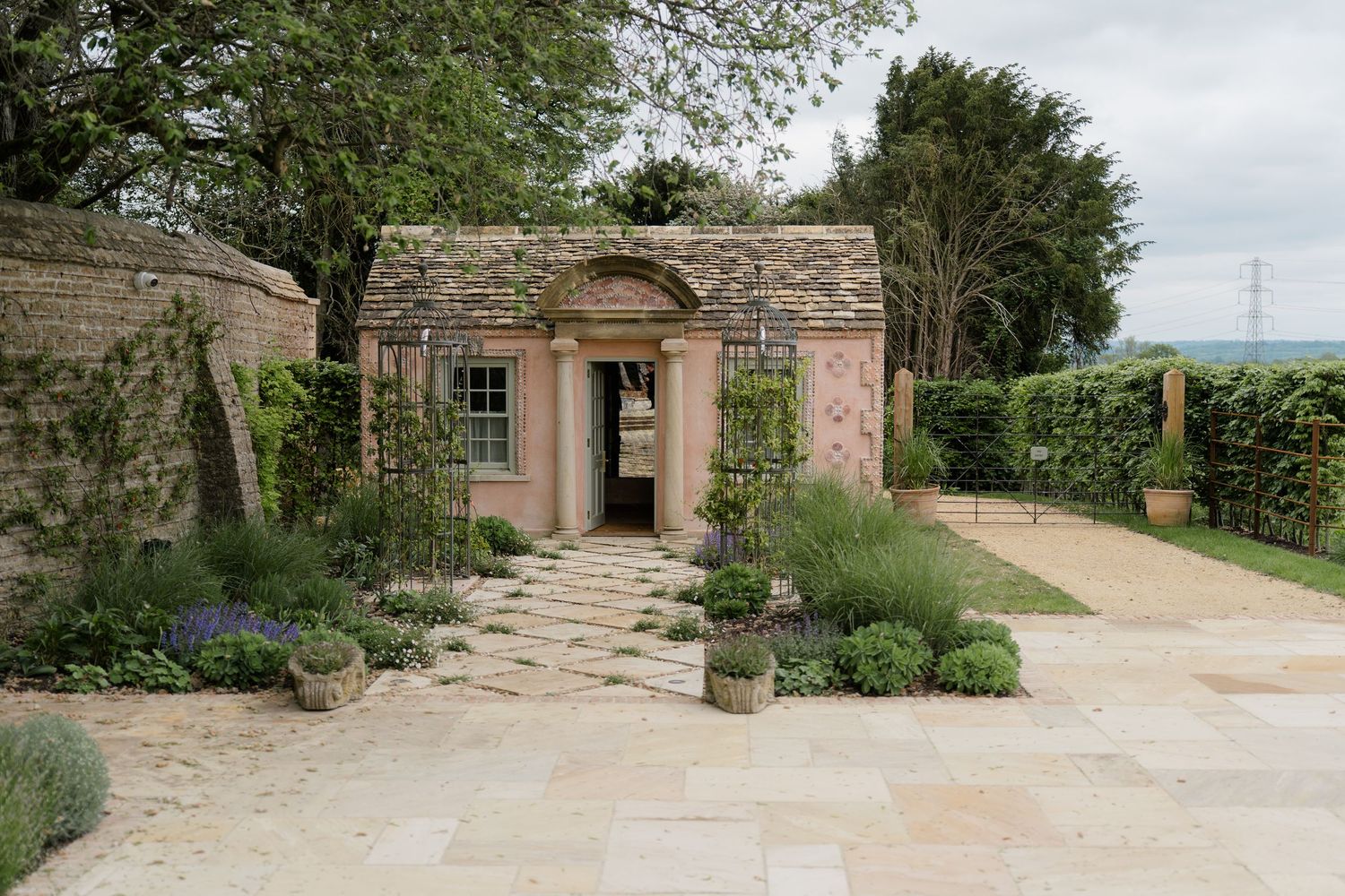 A charming stone garden pavilion with arched entrance surrounded by manicured hedges and lavender.
