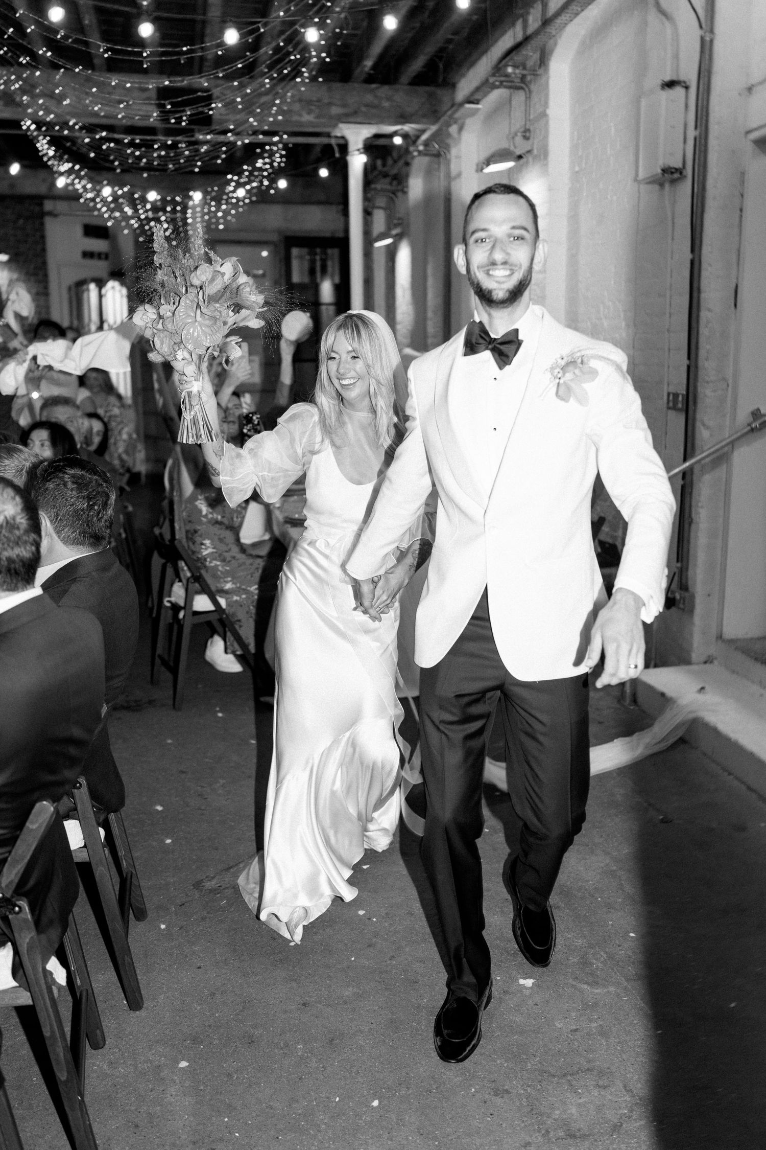 Wedding party runs through confetti during an indoor celebration.