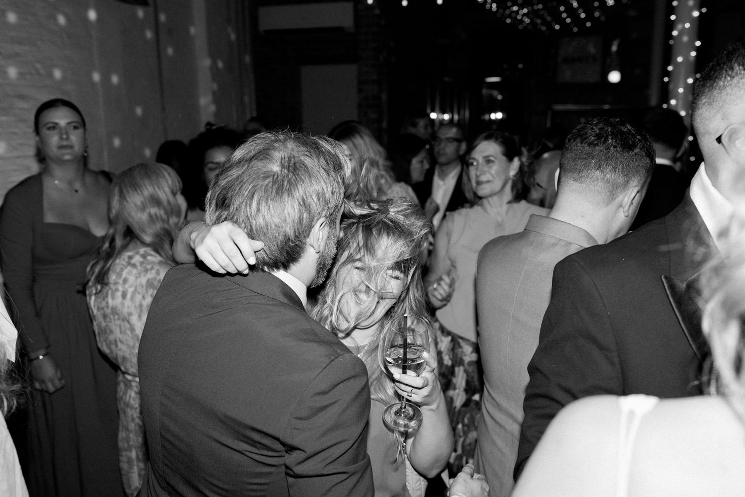 Wedding guests dancing and celebrating at a dimly lit reception.