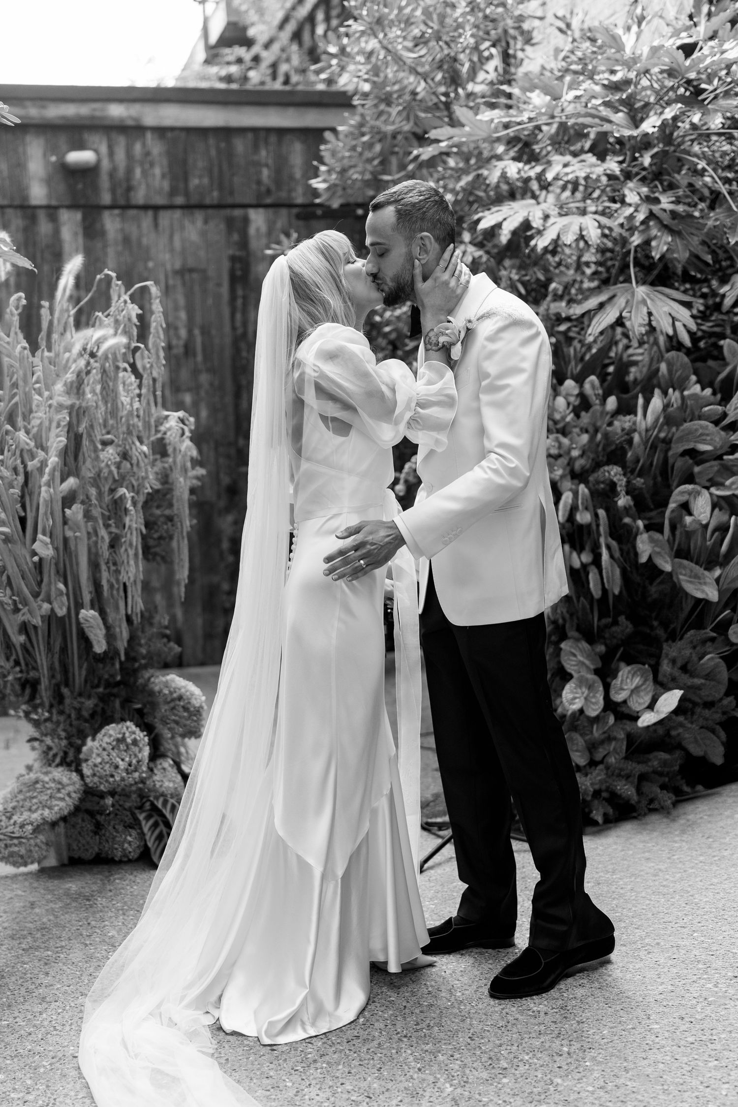 Wedding party members in white dresses and formal attire gather on a garden pathway.