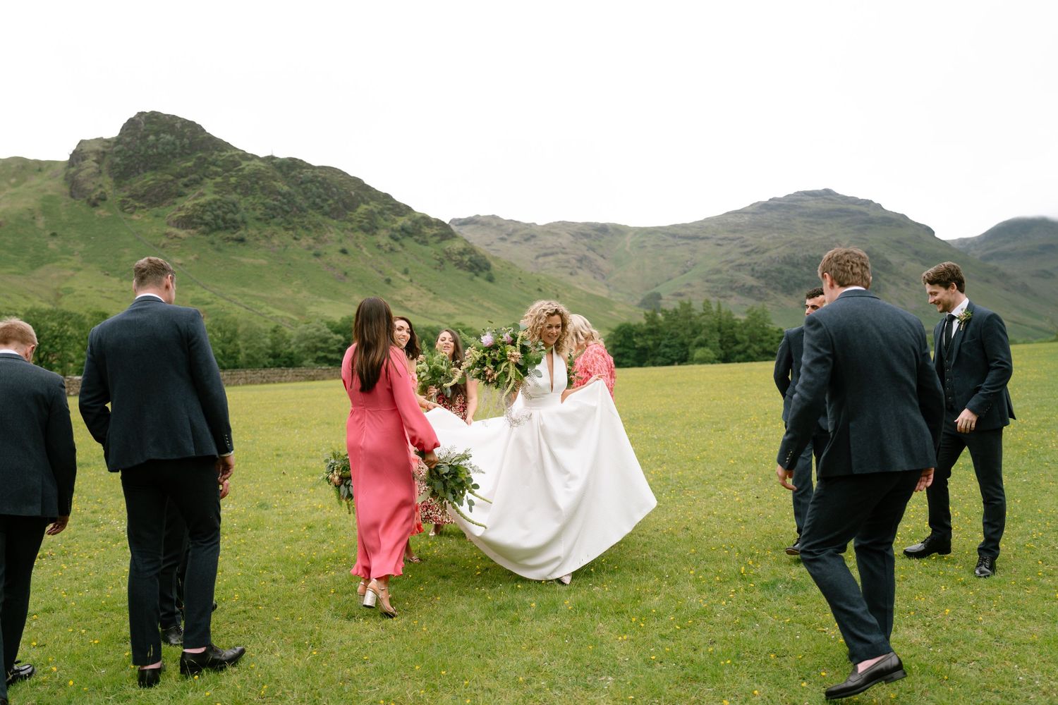 Wedding party walking across green hillside landscape.